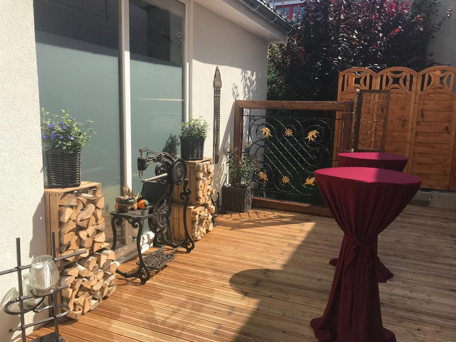 Sonnige Holzterrasse im Innenhof mit alter Sattlernähmaschine, Brennholz und Stehtischen für Feiern