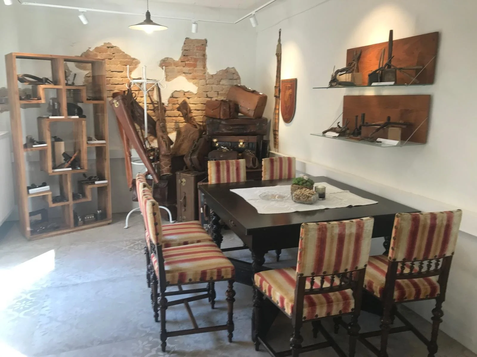 Gedeckter Tisch mit antiken Stühlen im Sattlermuseum Winklmayr, dahinter alte Lederkoffer und Werkzeuge