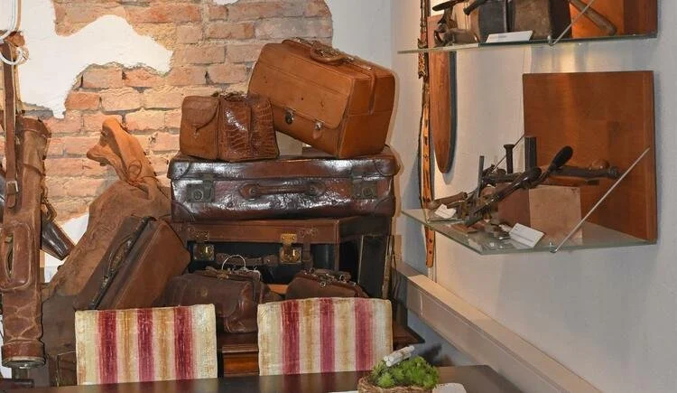 Gestapelte alte Lederkoffer und Arztkoffer vor einer freigelegten Ziegelwand, daneben Werkzeug auf Glasborden