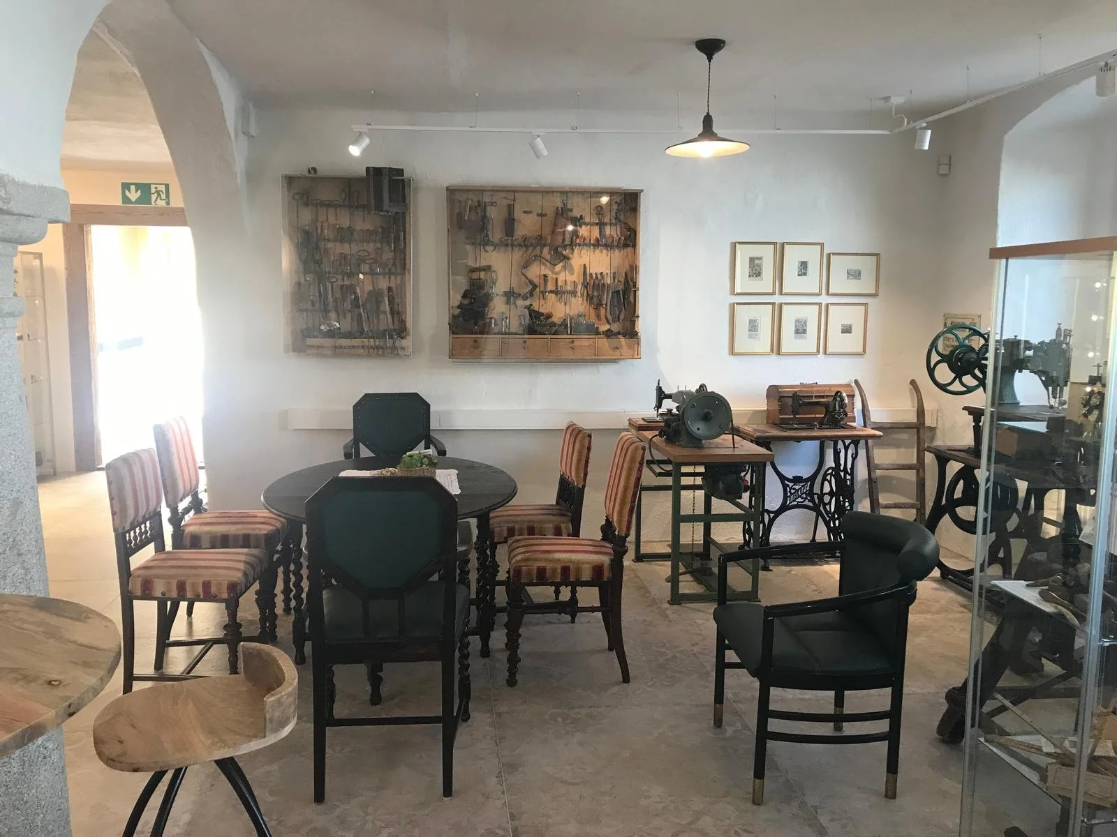 Ausstellungsraum mit Tischen und antiken Stühlen, im Hintergrund Werkzeugtafeln und Nähmaschinen