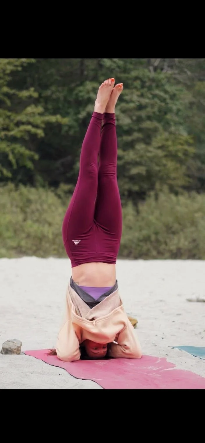 Femme pratiquant la tête à l'envers sur un tapis de yoga en extérieur avec un fond naturel d'arbres.