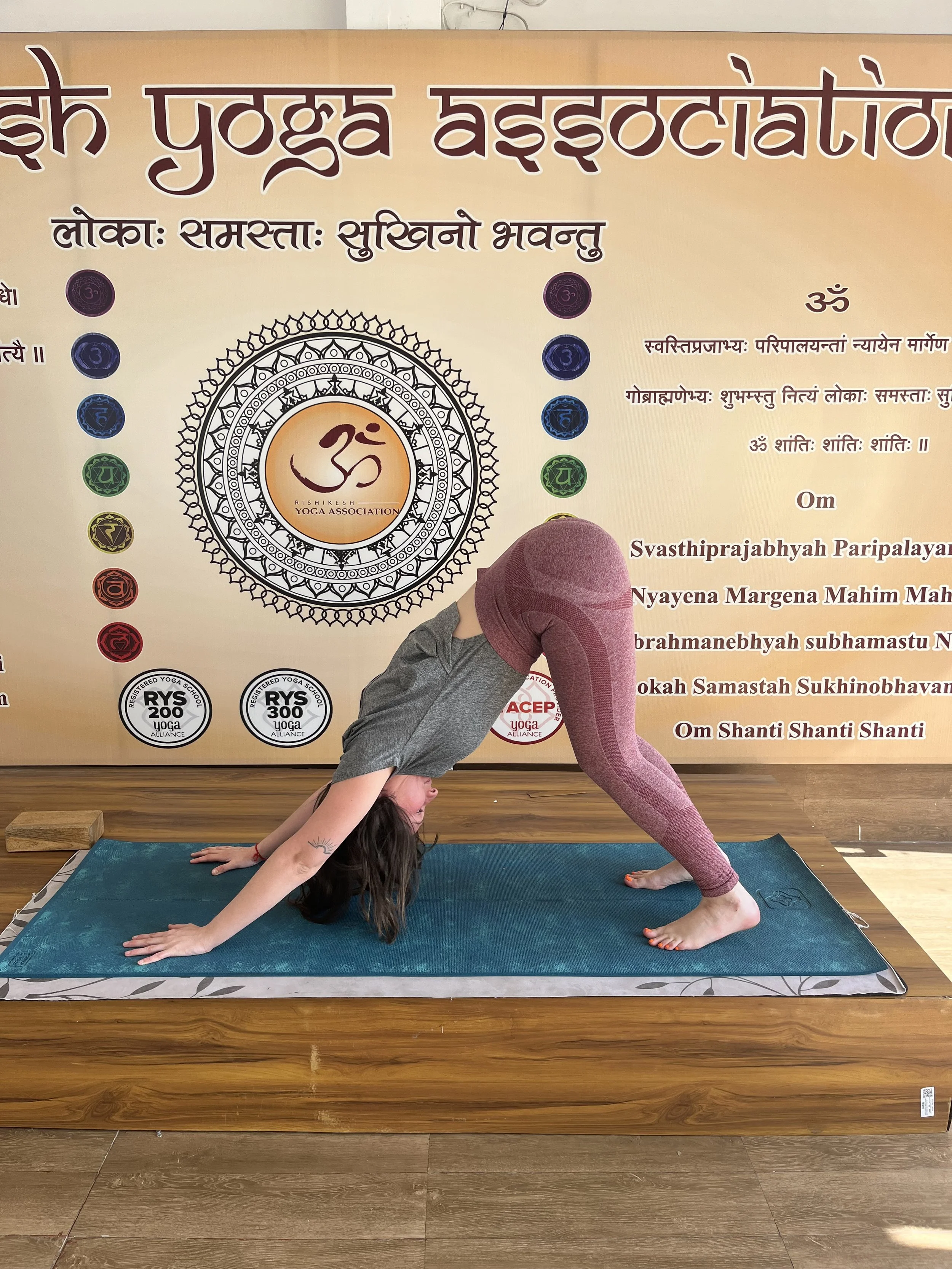 Une femme en position de yoga, en équilibre inversé avec les mains au sol et une jambe levée, dans une salle de yoga avec un panneau sur le mur derrière elle.