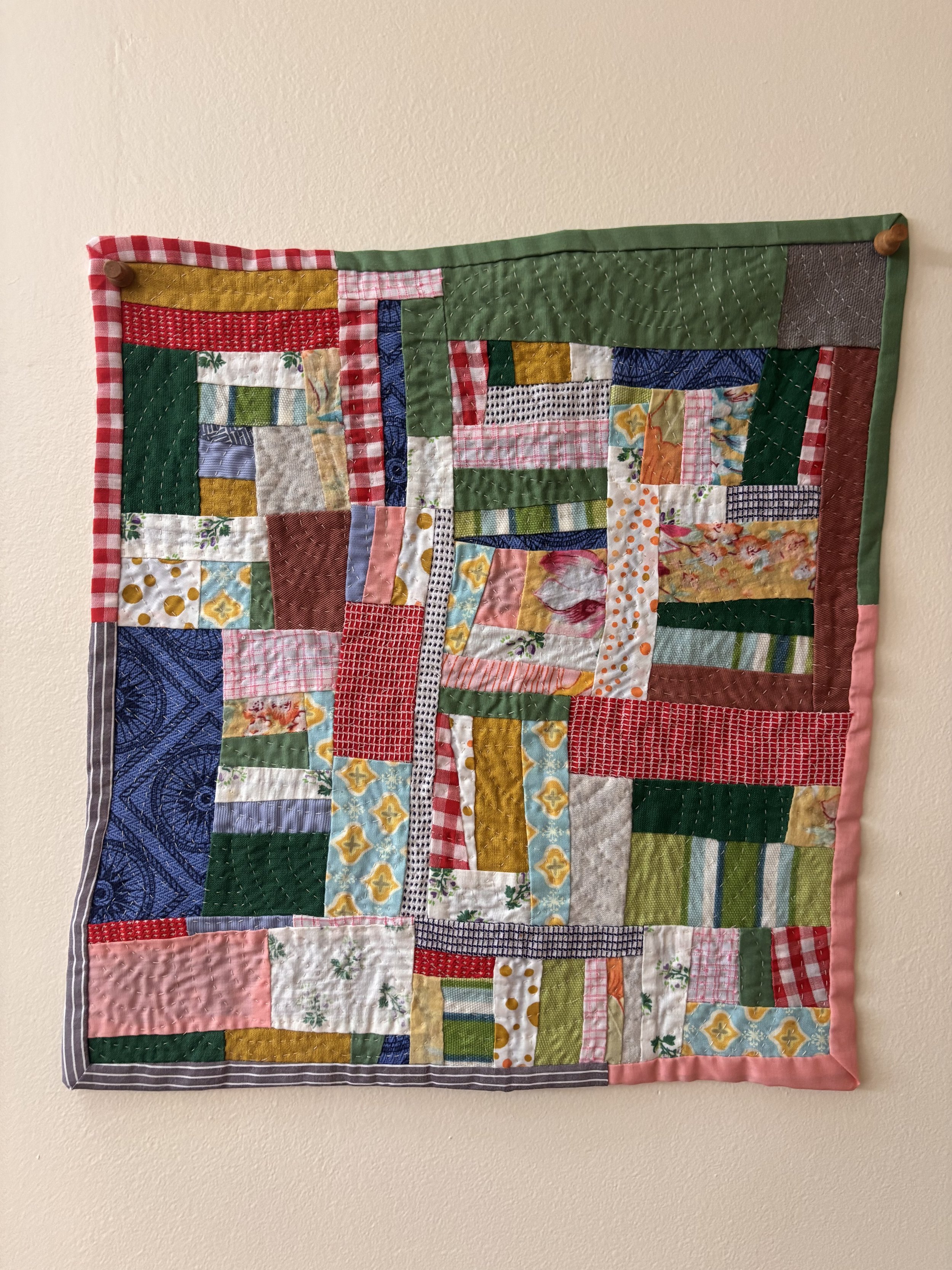 Colorful handmade patchwork quilt wall hanging with stitched fabric squares and wooden pegs
