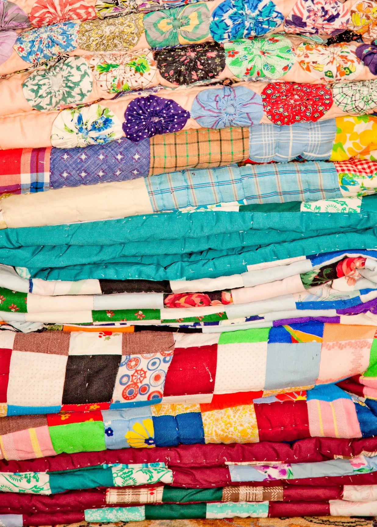 Stack of colorful handmade patchwork quilts and floral fabric pieces