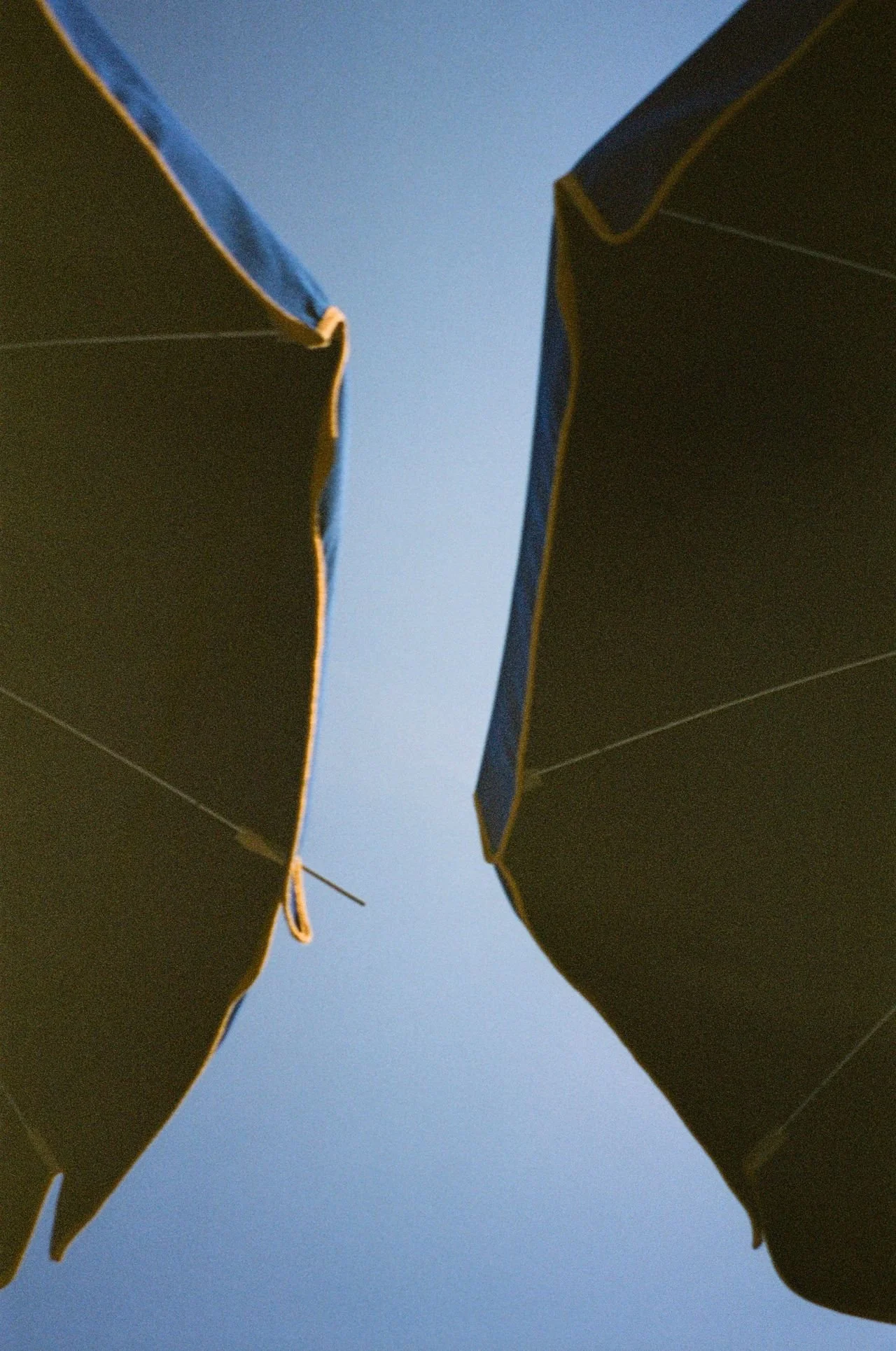 Close-up of two umbrellas opened and positioned opposite each other, with a clear blue sky in the background.