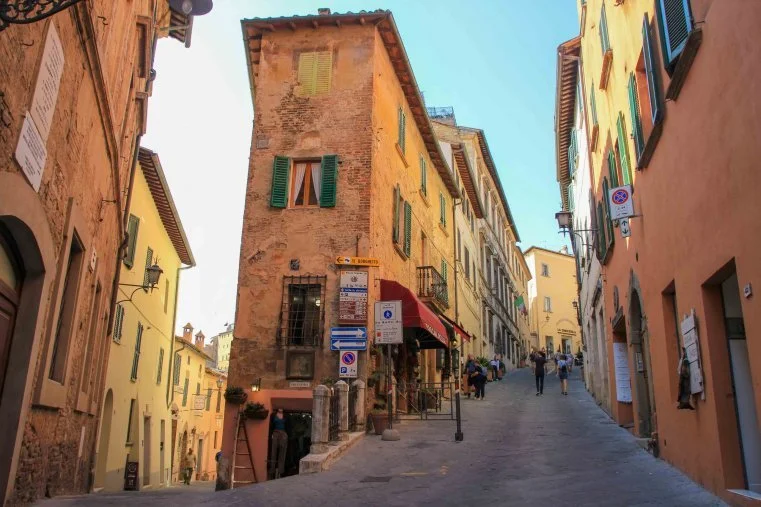 Tall, narrow buildings with colorful facades and shuttered windows on a hilly street in Montepulciano.