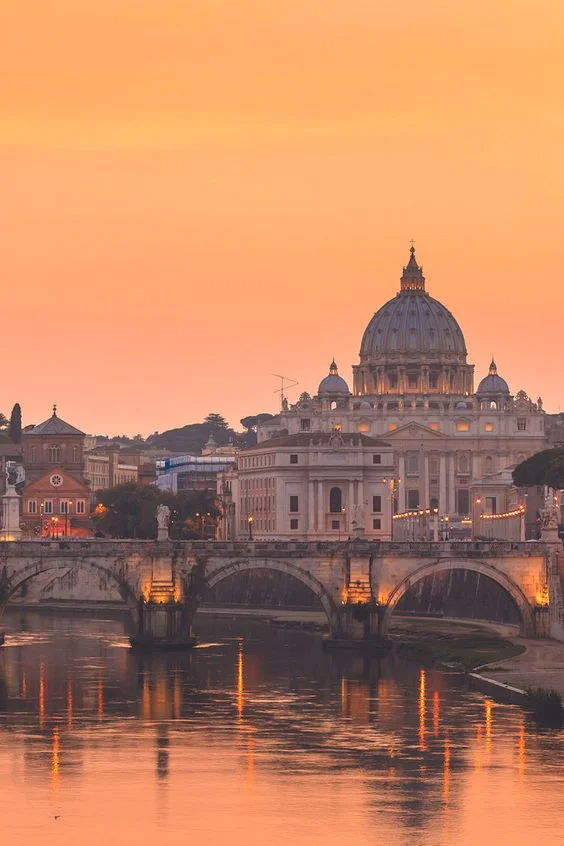 View of St. Peter's Basilica illuminated at sunset, reflected in the Tiber River in Rome, Italy.