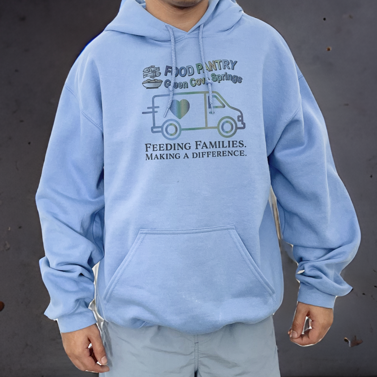 Person wearing a light blue hoodie with a logo for a food pantry and the slogan "Feeding Families. Making a Difference."