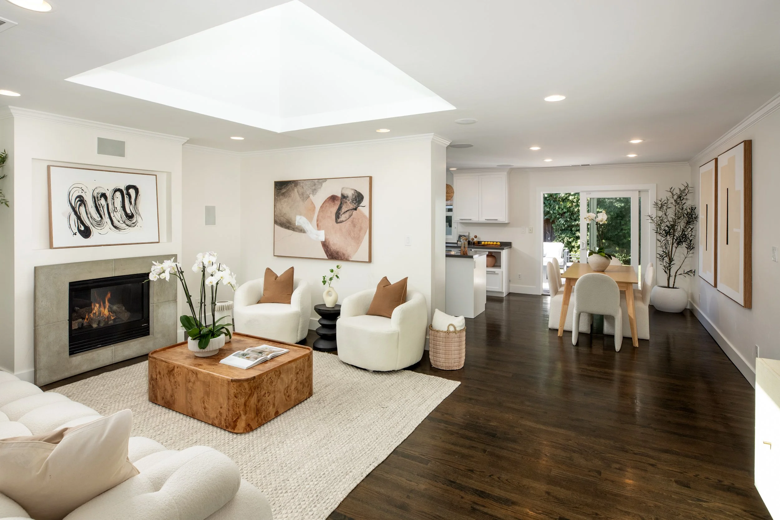 Living room with white furniture, a fireplace, wall art, and a dining area near a sliding glass door leading outside.