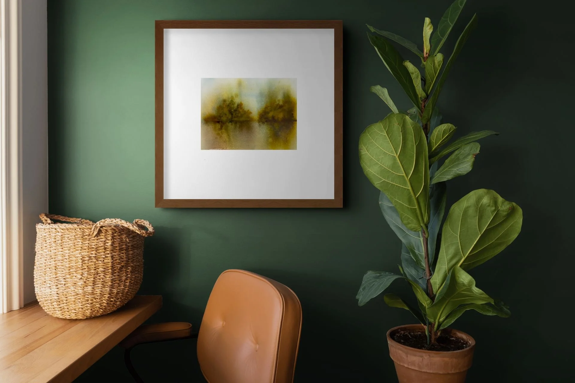 Stylish home office with framed abstract landscape art, woven basket on a wooden desk, tan chair, and large potted fiddle-leaf fig against a dark green wall