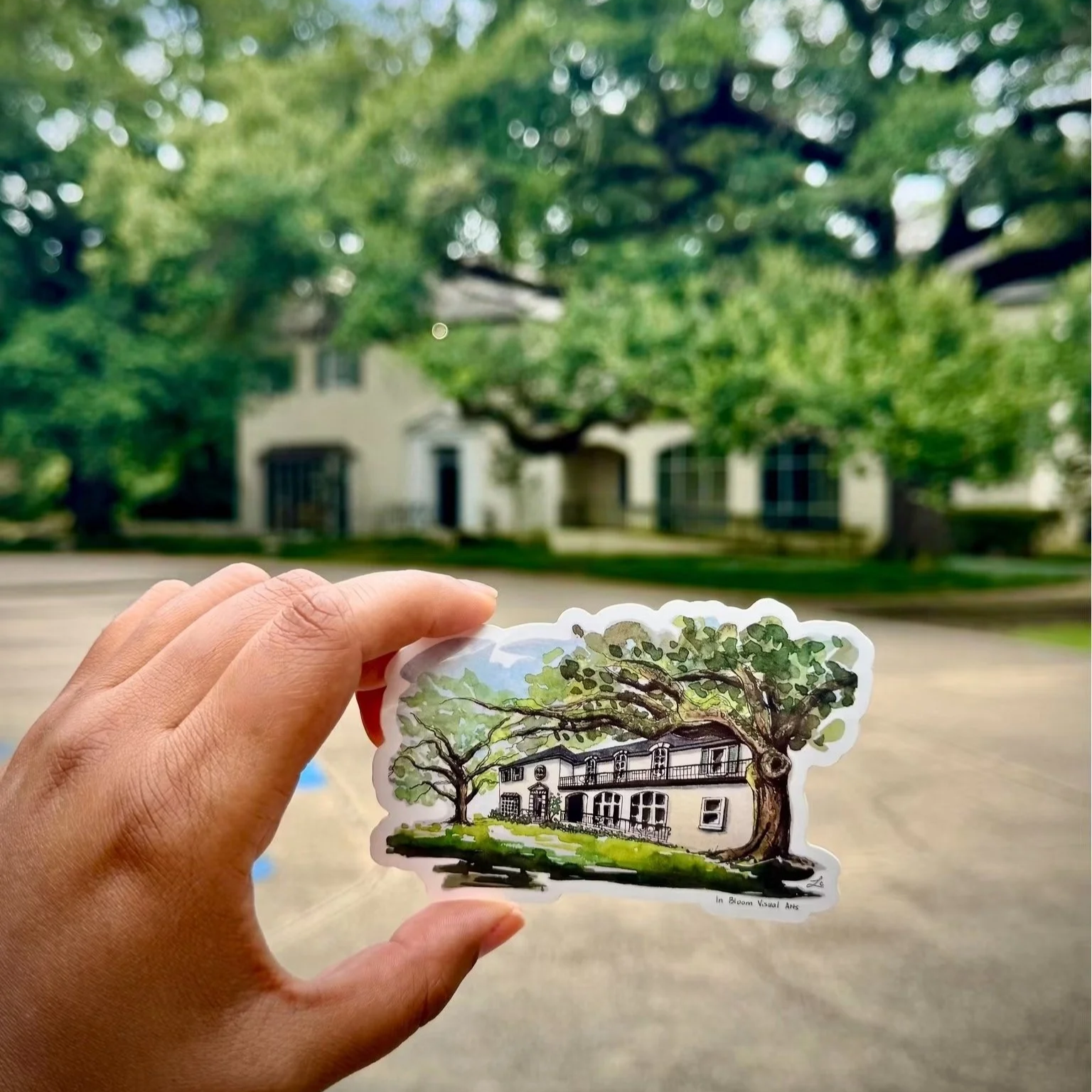 Hand holding a watercolor house sticker aligned with a real house in the background