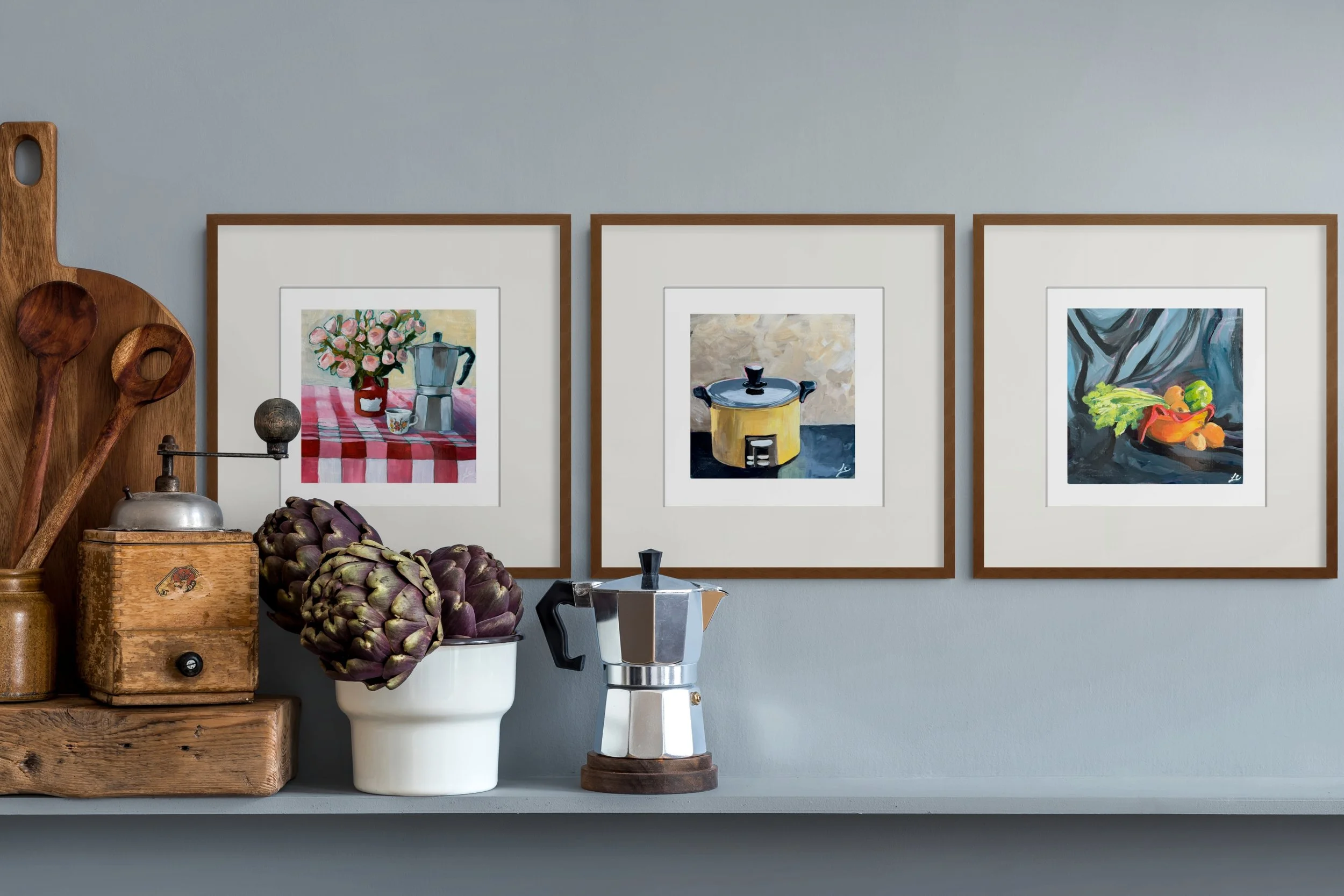 Still life kitchen display with artichokes, moka pot, wooden utensils, and three framed food paintings