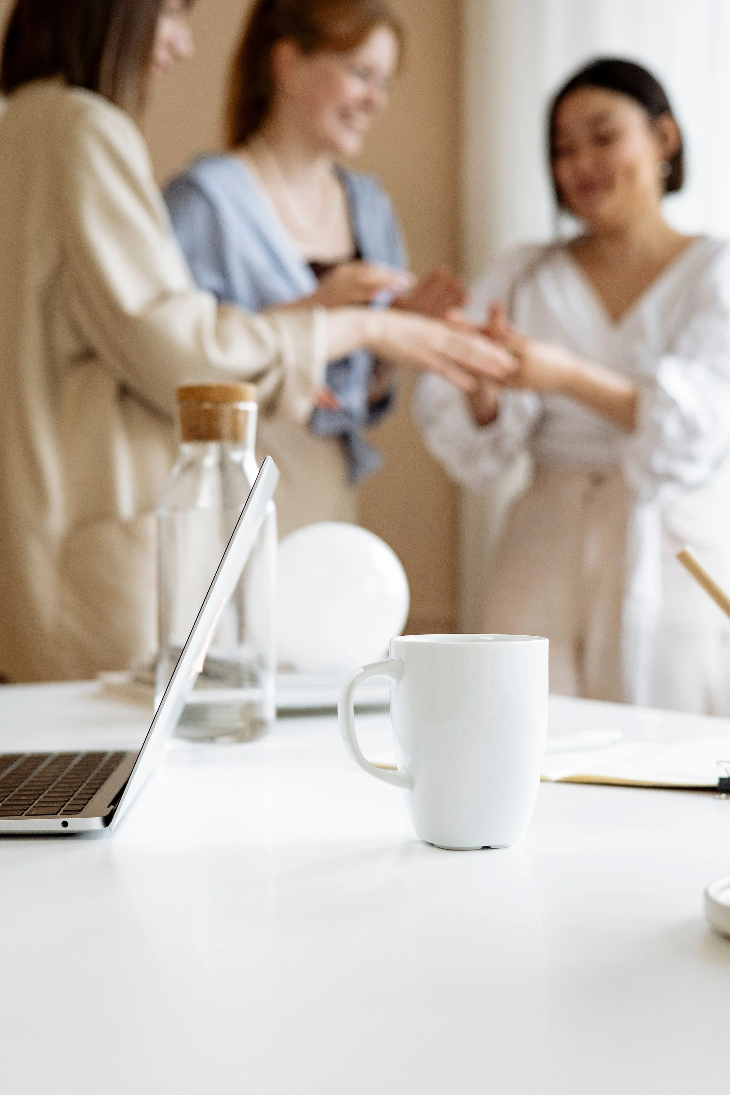 Blurred business meeting with three coworkers around a table, laptop, white coffee mug, and notebook