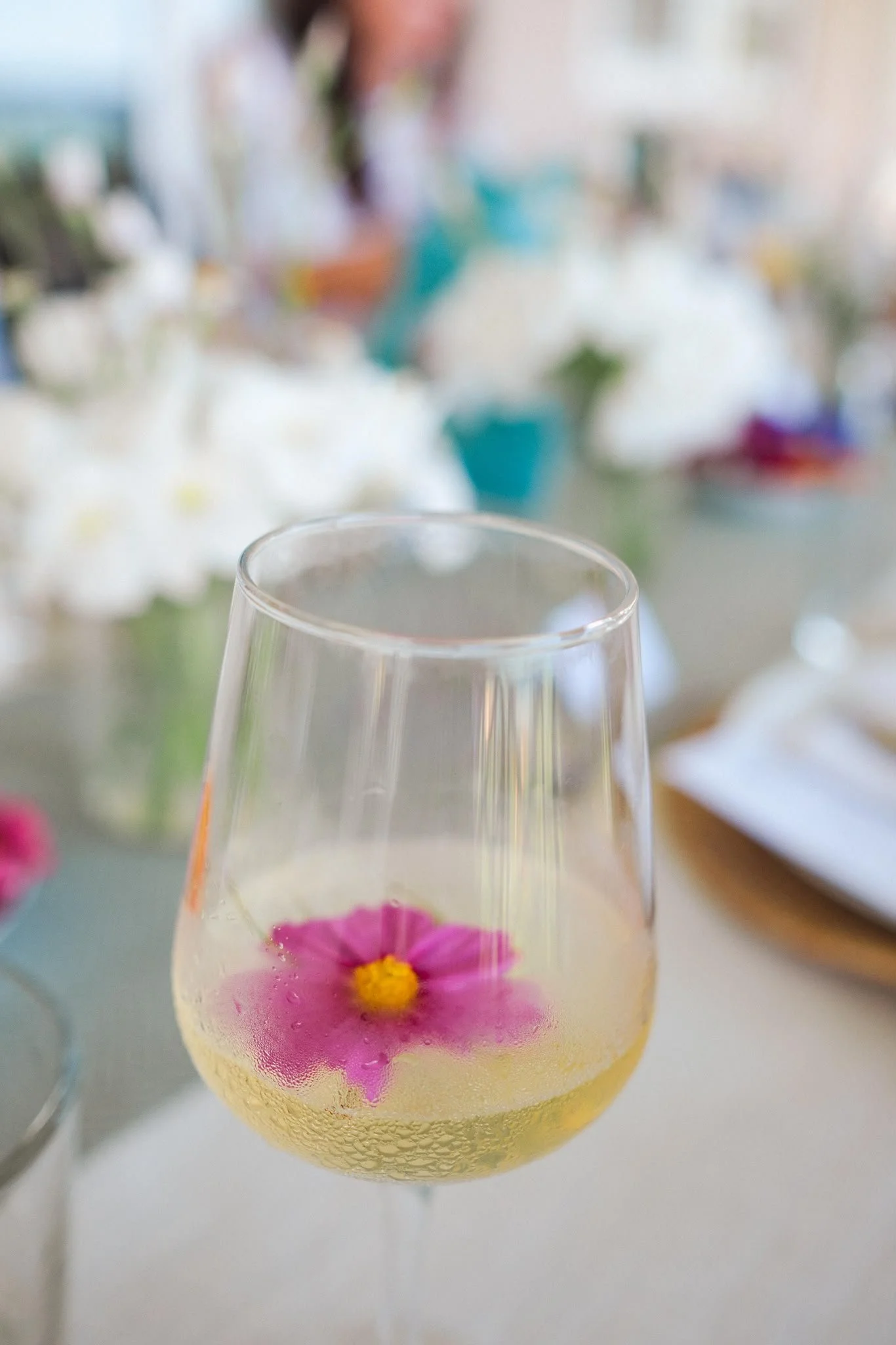 Clear glass of pale sparkling wine garnished with a pink flower on a table
