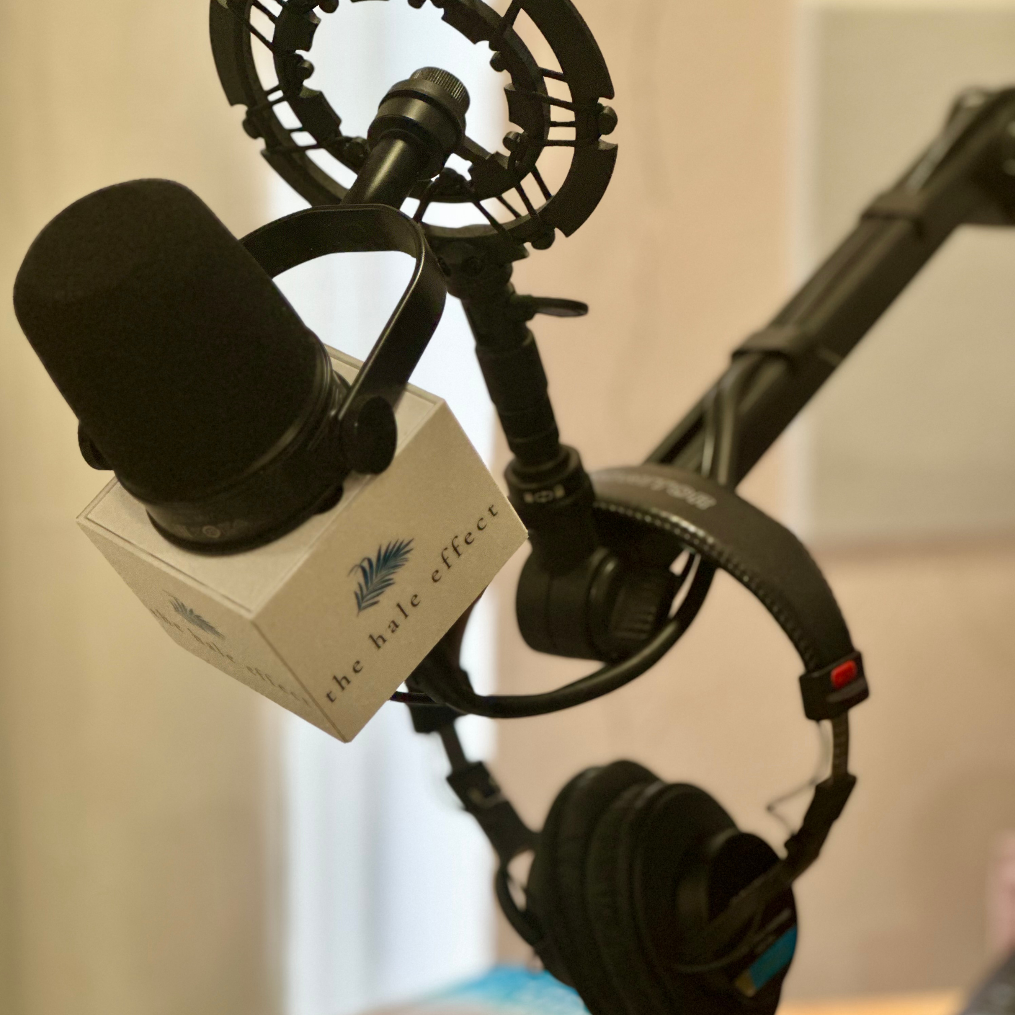 Close-up of a black studio microphone with pop filter, shock mount, and headphones on a boom arm