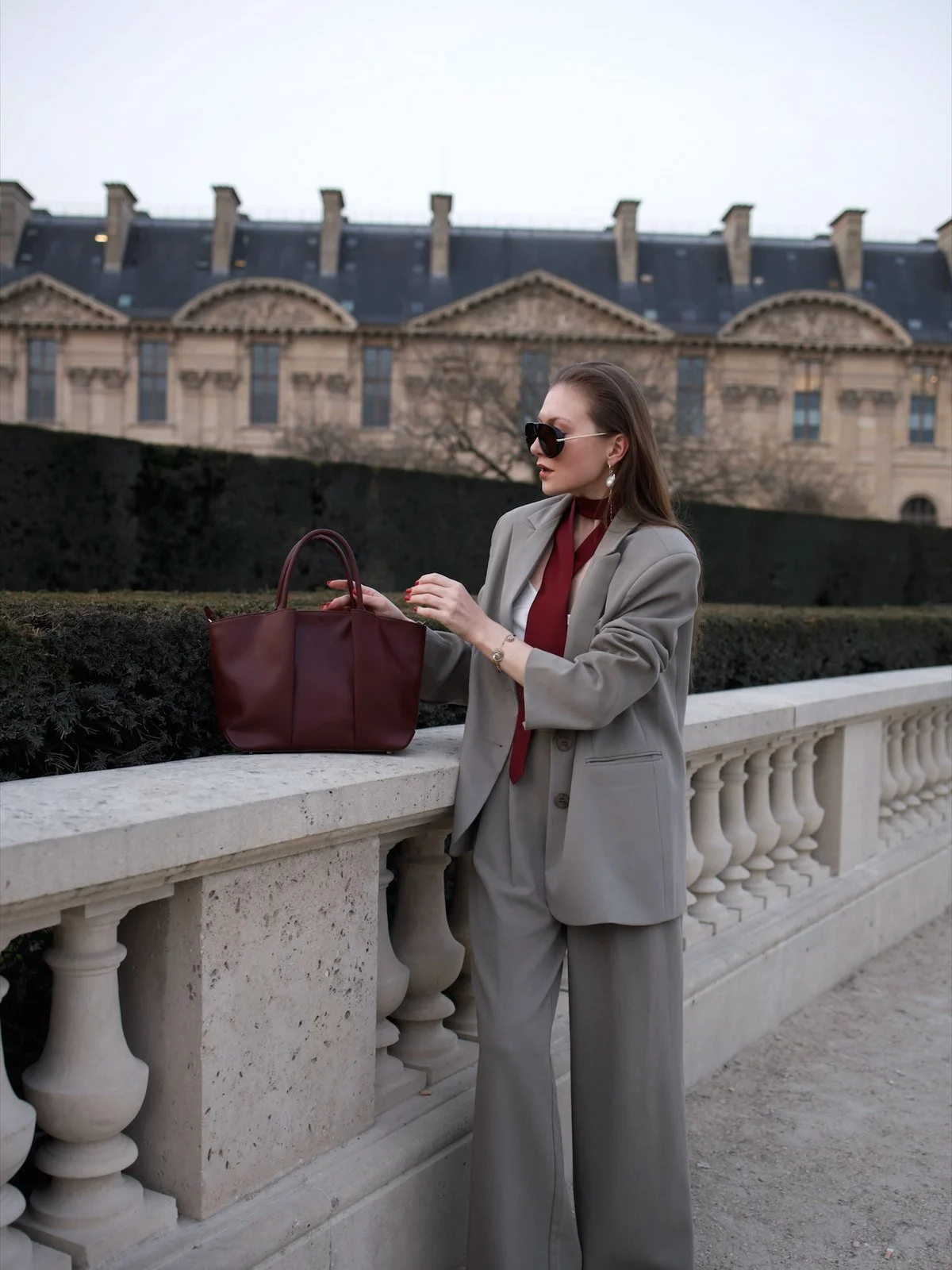 Emily Varr in a grey suit with a burgundy KAAI bag at Paris Fashion Week
