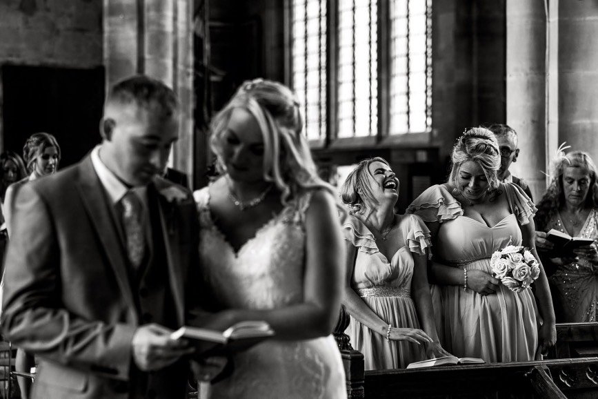 Black-and-white wedding ceremony inside a historic church, with the bride and groom in the foreground and bridesmaids standing behind them.