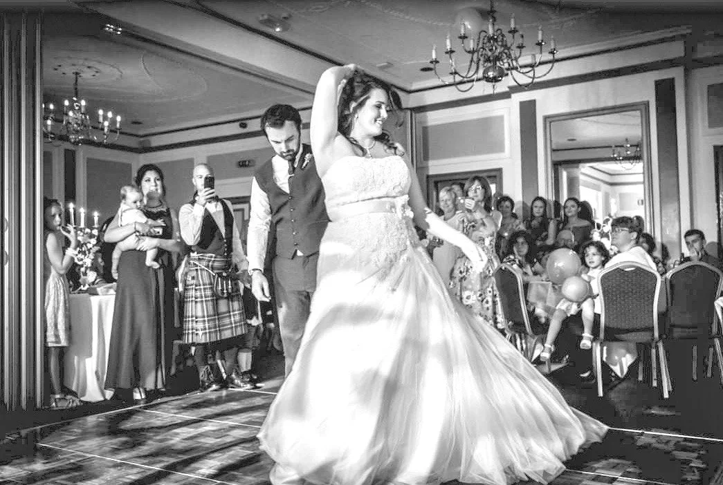 Bride and groom dancing at a wedding reception as guests watch and take photos.