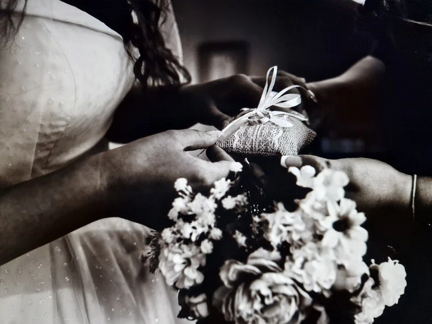 Black-and-white wedding photo of a bride holding a lace ring pillow and floral bouquet