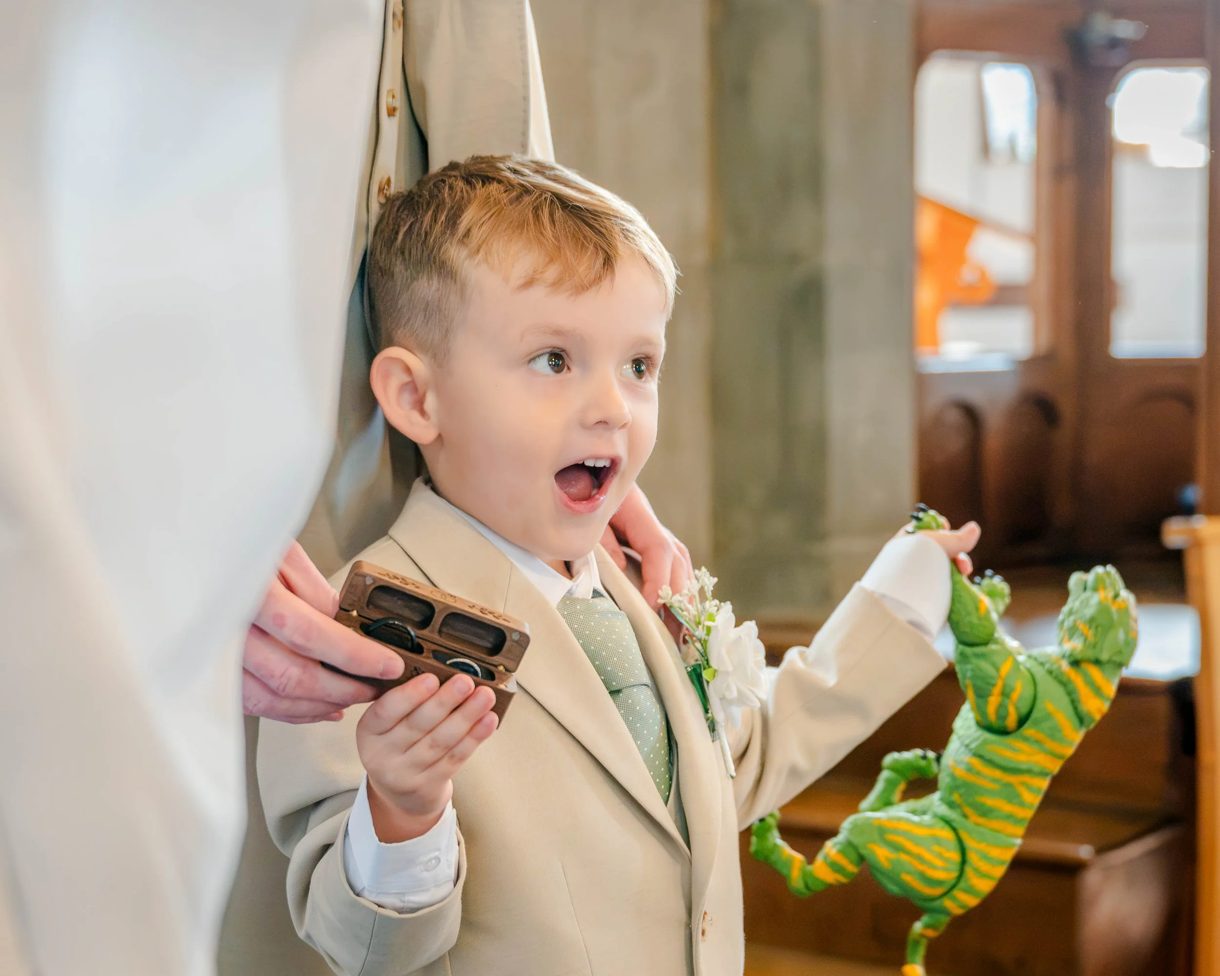 Young boy in a cream suit and tie holding a bouquet of greenery and flowers at a wedding