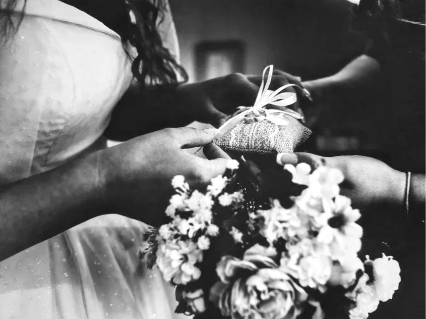 Black-and-white close-up of a bride holding a ribbon-wrapped wedding gift and bouquet of flowers
