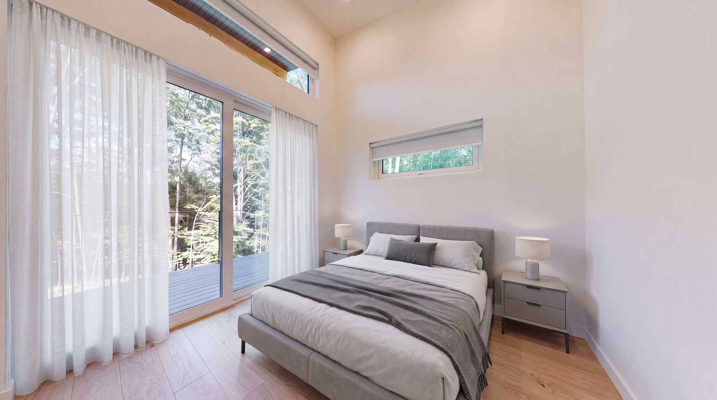 Modern minimalist bedroom with a gray upholstered bed, bedside tables and lamps, floor-to-ceiling windows, and forest views