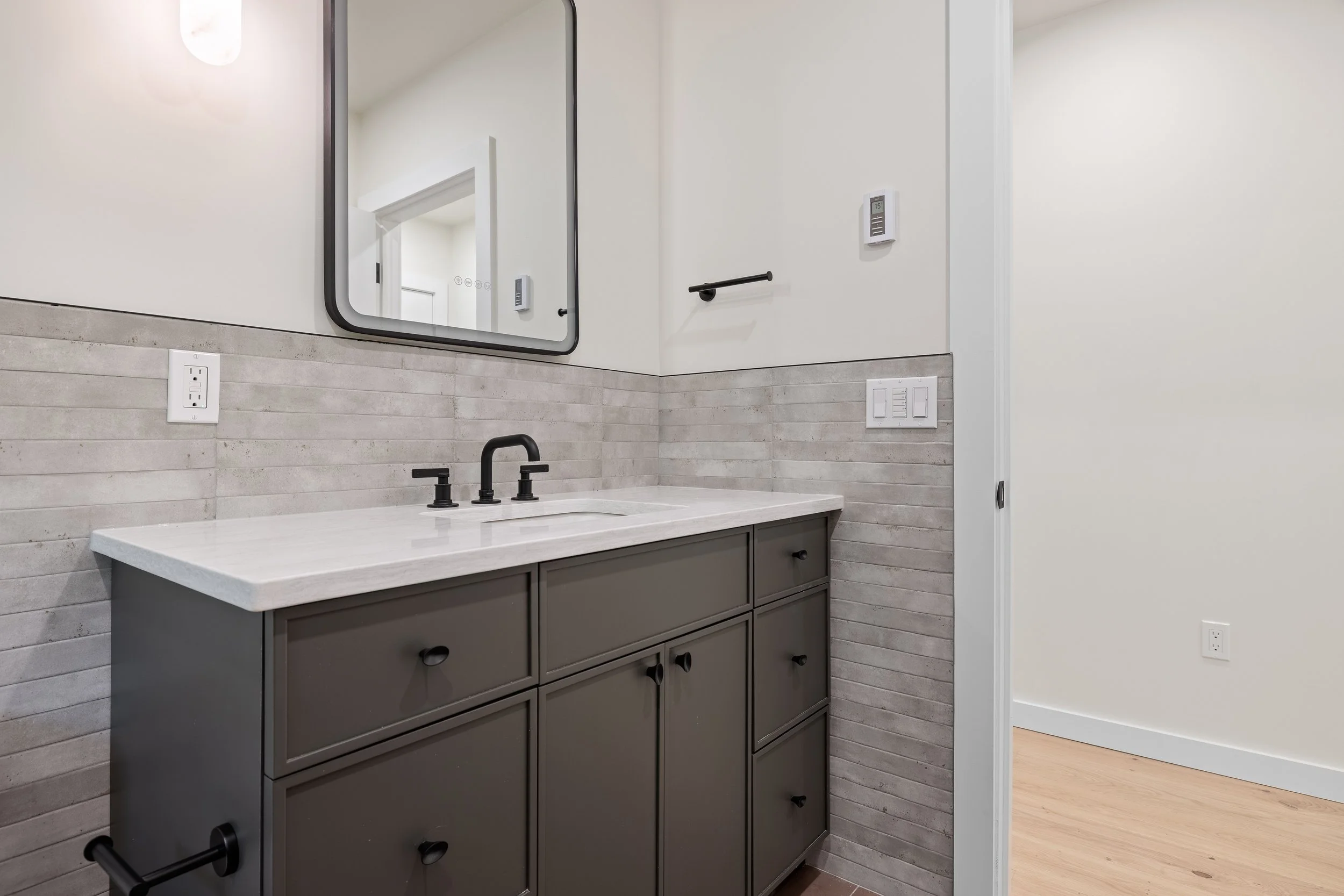 Modern bathroom vanity with dark gray cabinets, white countertop, black faucet, large mirror, and gray tile backsplash