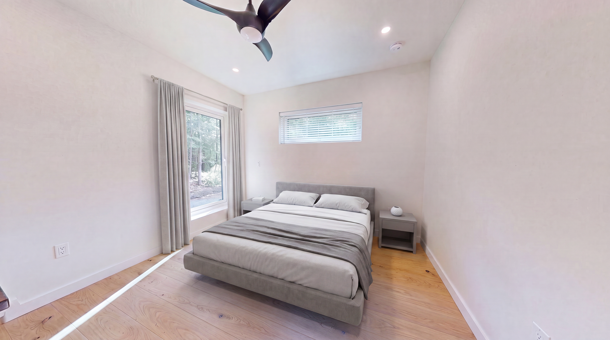 Bright minimalist bedroom with a gray upholstered bed, white bedding, nightstands, wood floors, windows, and a ceiling fan