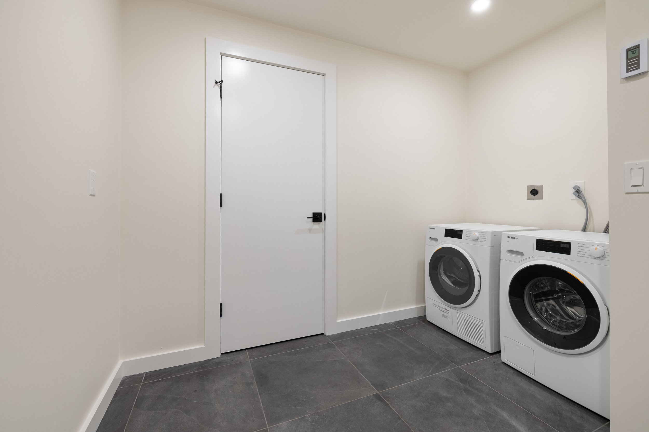 Modern laundry room with white Miele washer and dryer, tiled floor, and white door