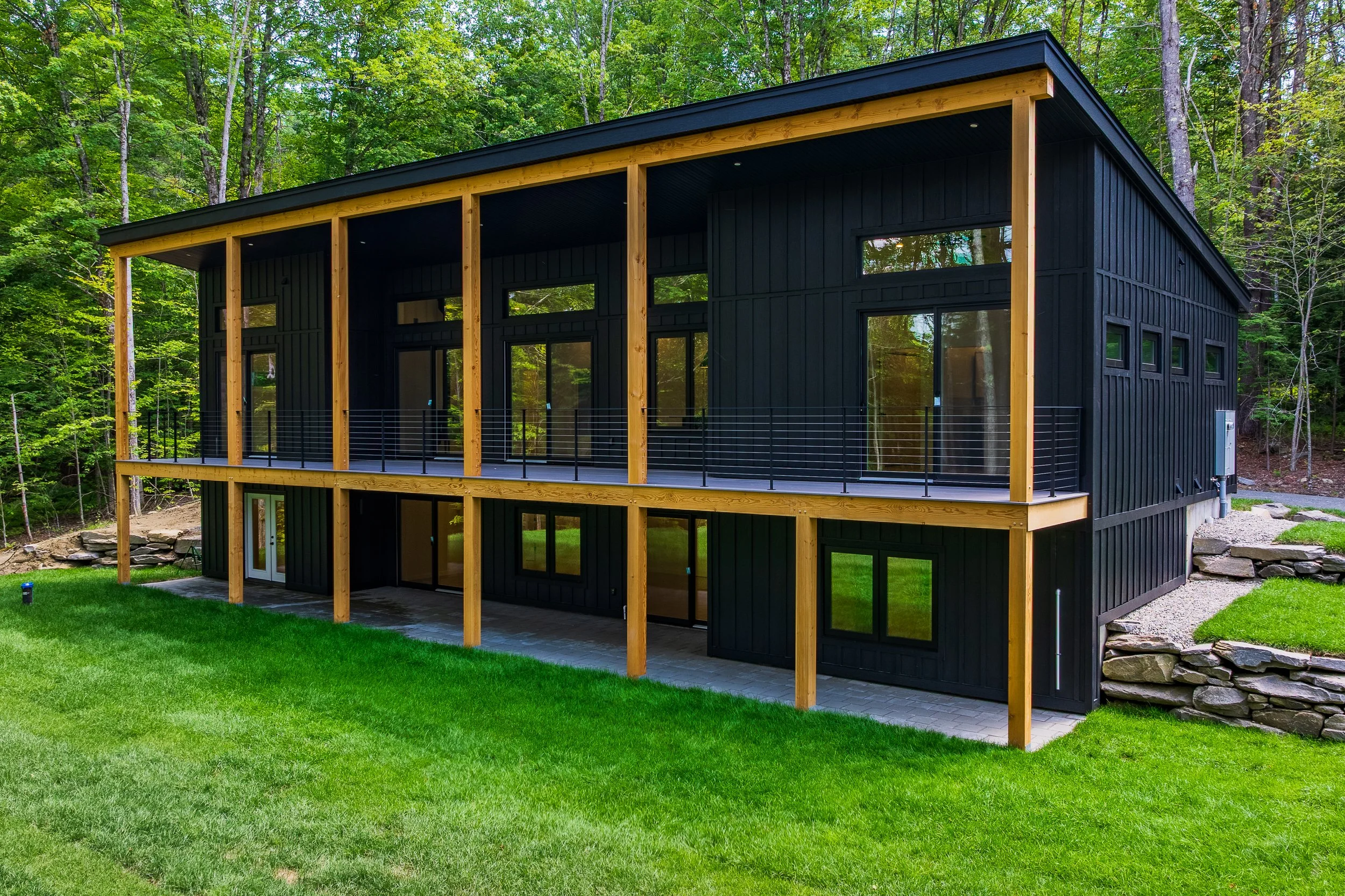 Modern black-sided cabin with a covered wooden deck in a forested setting