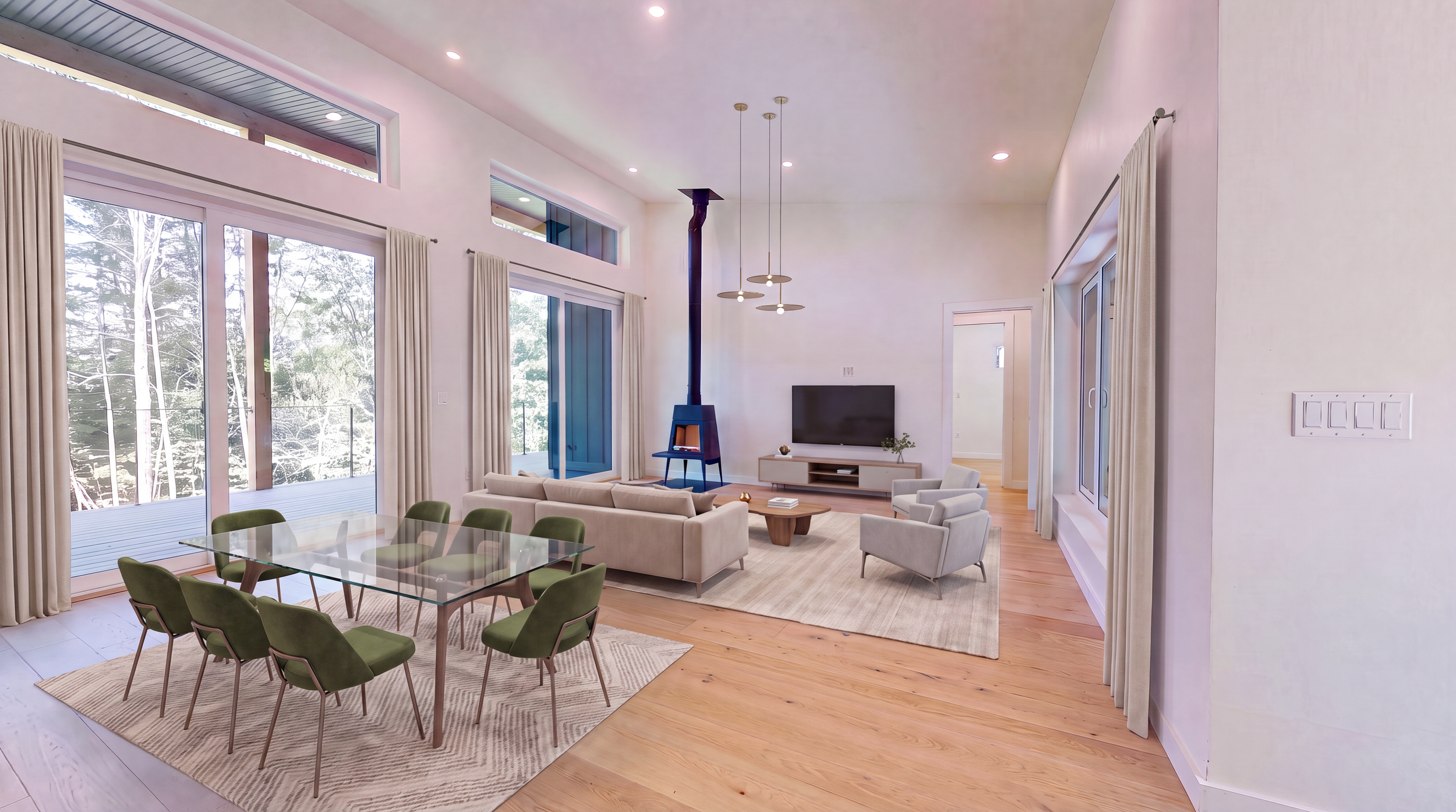 Modern open-plan living and dining room with glass table, green chairs, sectional sofa, fireplace, television, pendant lights, and large windows overlooking trees