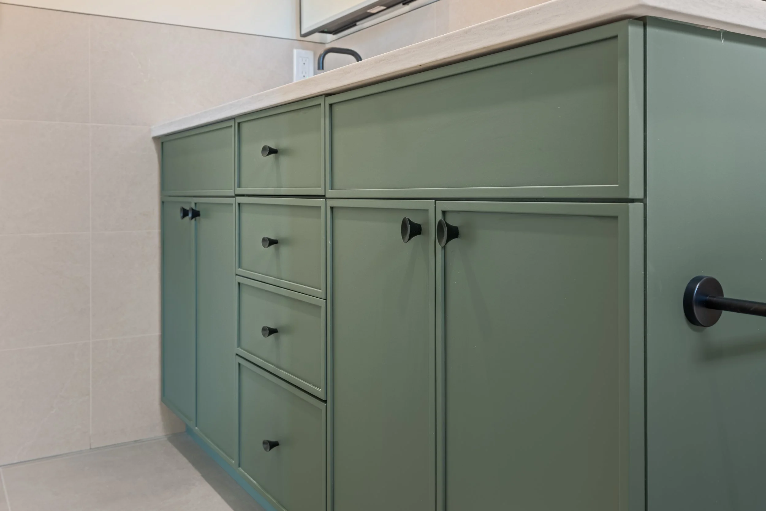 Sage green bathroom vanity with paneled cabinets, black hardware, and a light countertop