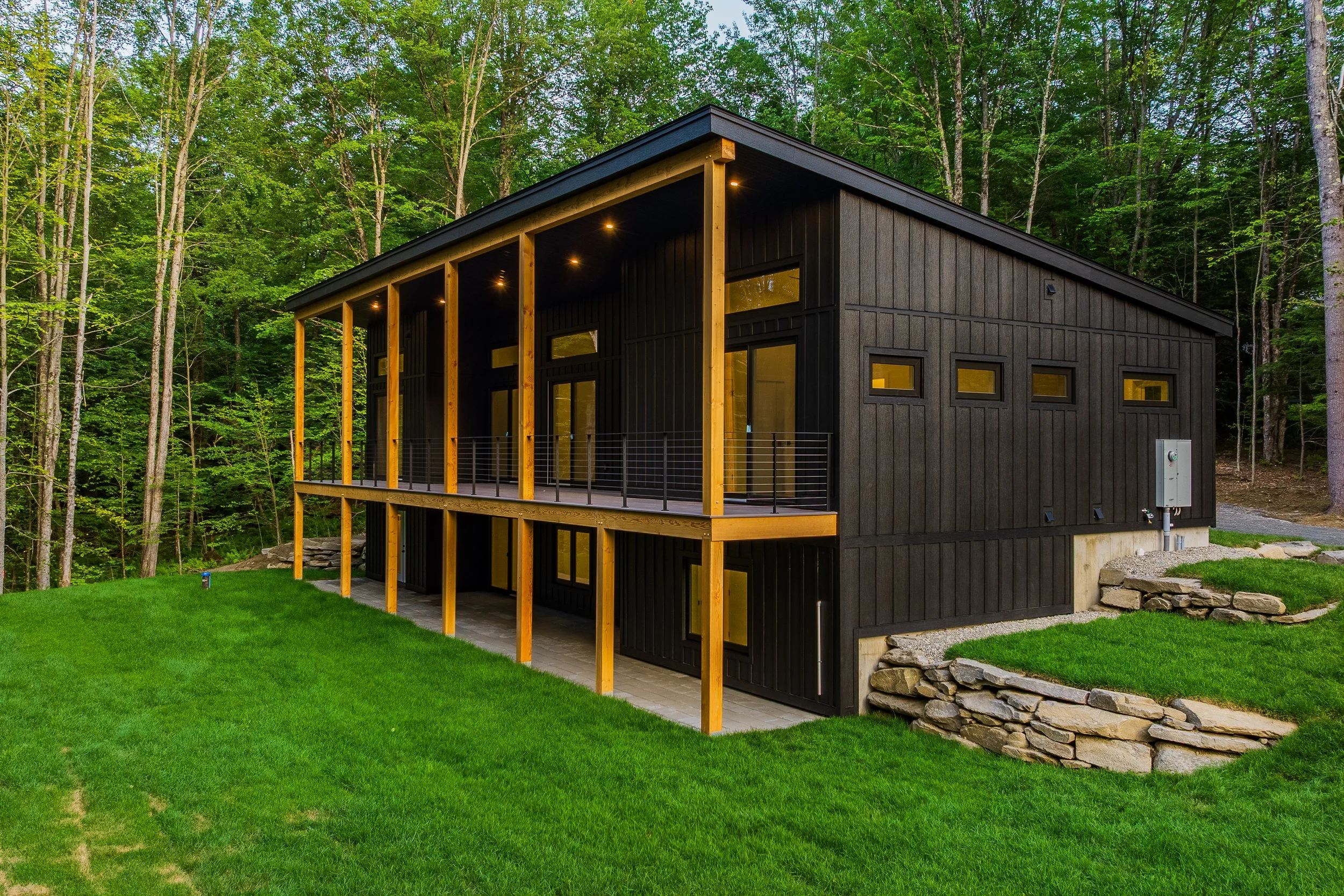 Modern black cabin with a covered wooden deck in a lush forest setting