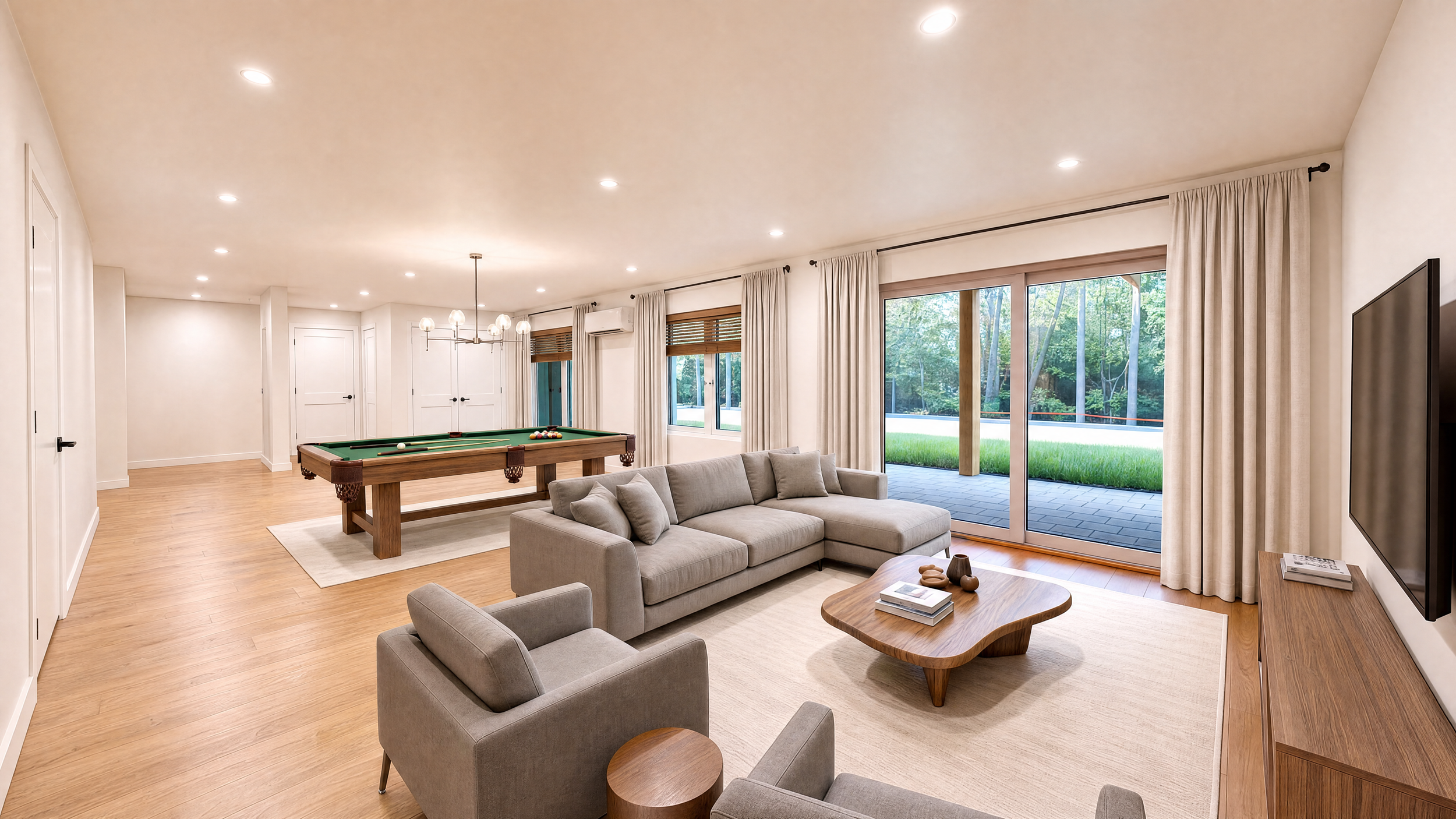 Modern open-plan living room with gray sectional sofa, pool table, wall-mounted TV, and sliding glass doors opening to a landscaped patio