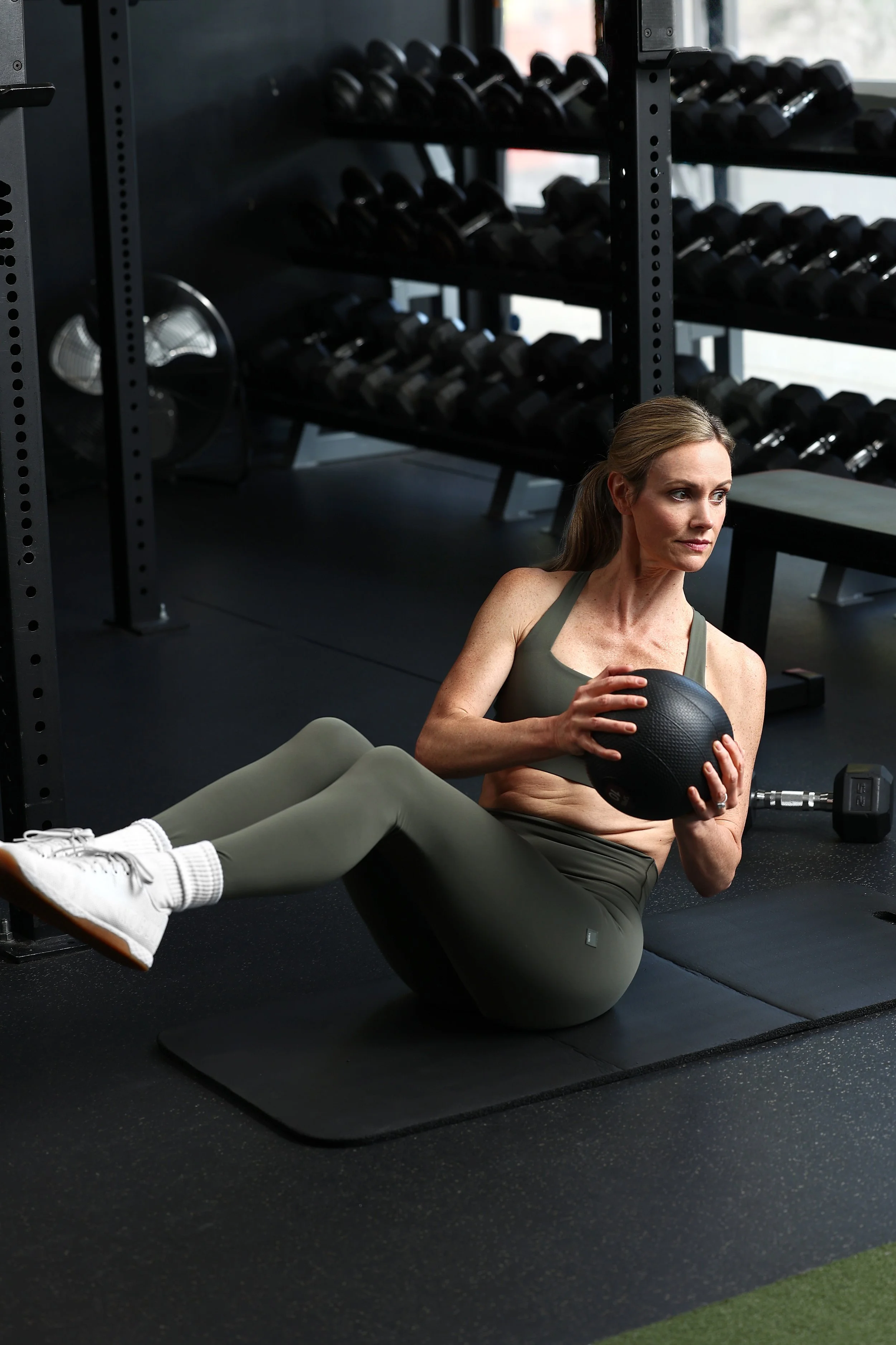 Stacie Carney wearing a green workout Vuori outfit performing Russian twists with a medicine ball during a core strength exercise.