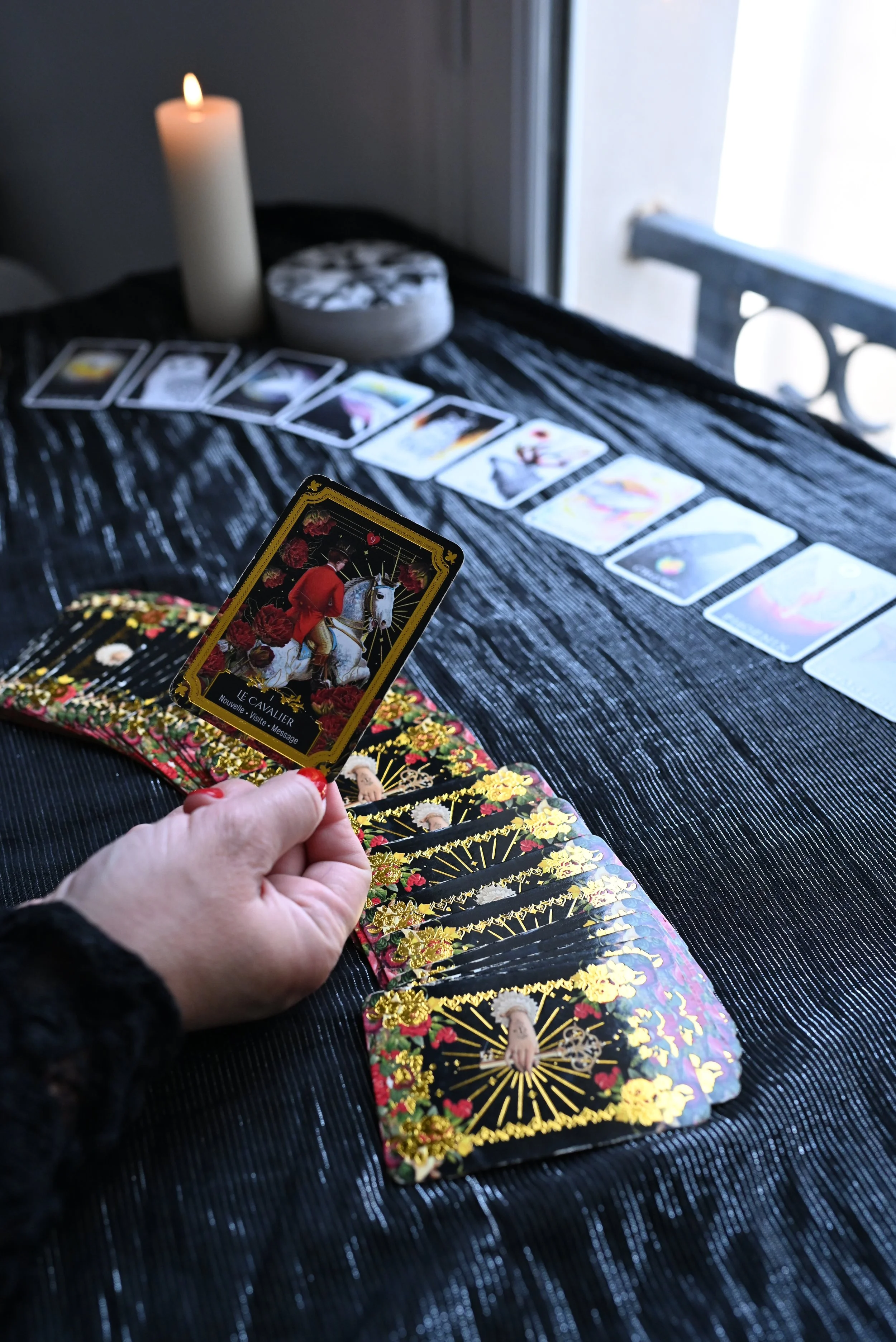 Hand holding a tarot card labeled Le Cavalier above a spread of cards, with a lit candle and crystal nearby.