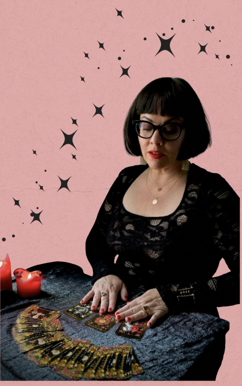 Woman fortune teller reading tarot cards at a table with candles against a pink star-patterned background