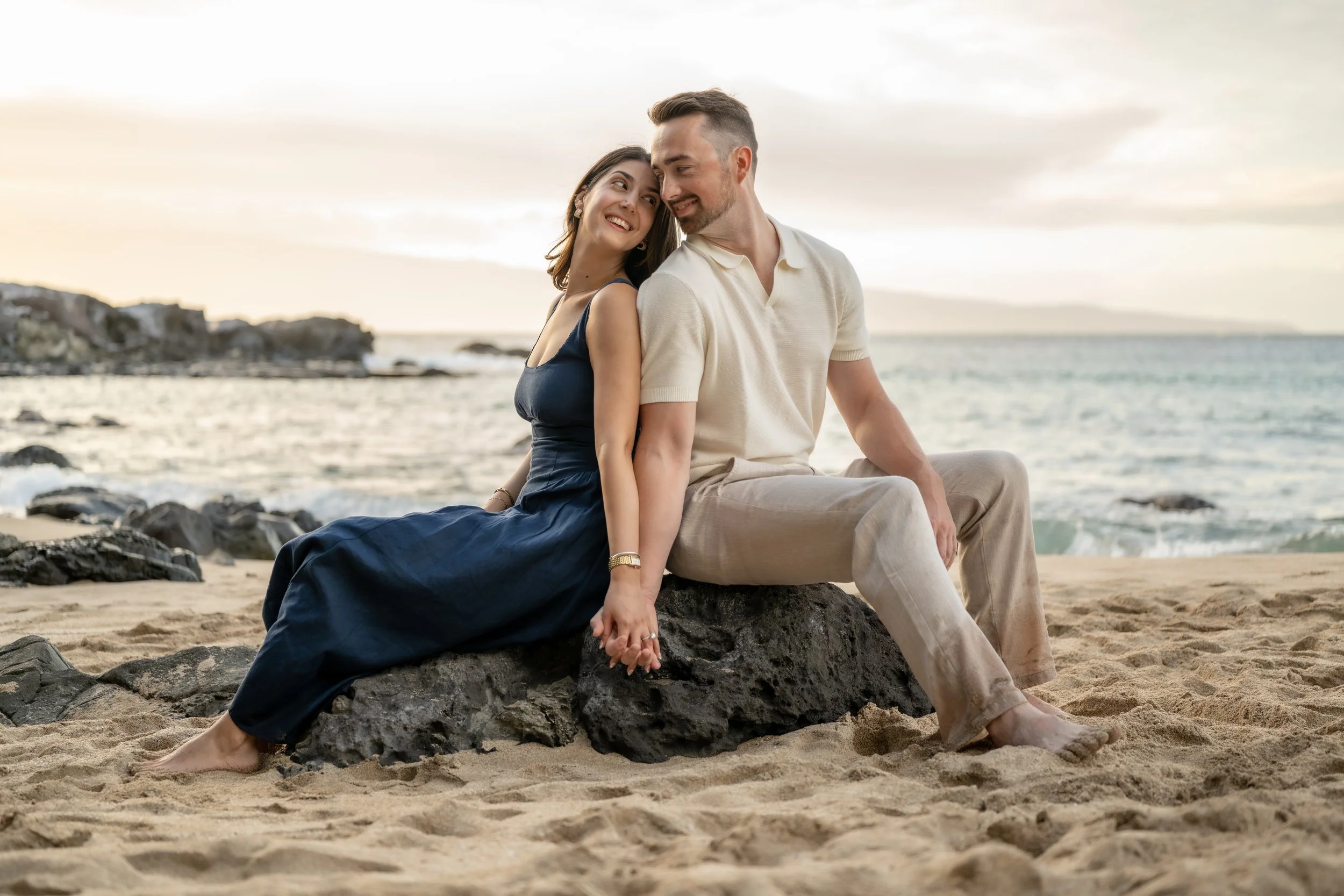 13. Couple sitting close together on a beach rock in warm evening light.