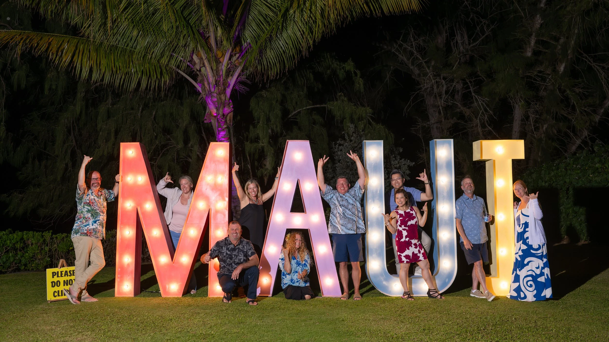 Guests posing beside illuminated MAUI letters at an outdoor evening event.