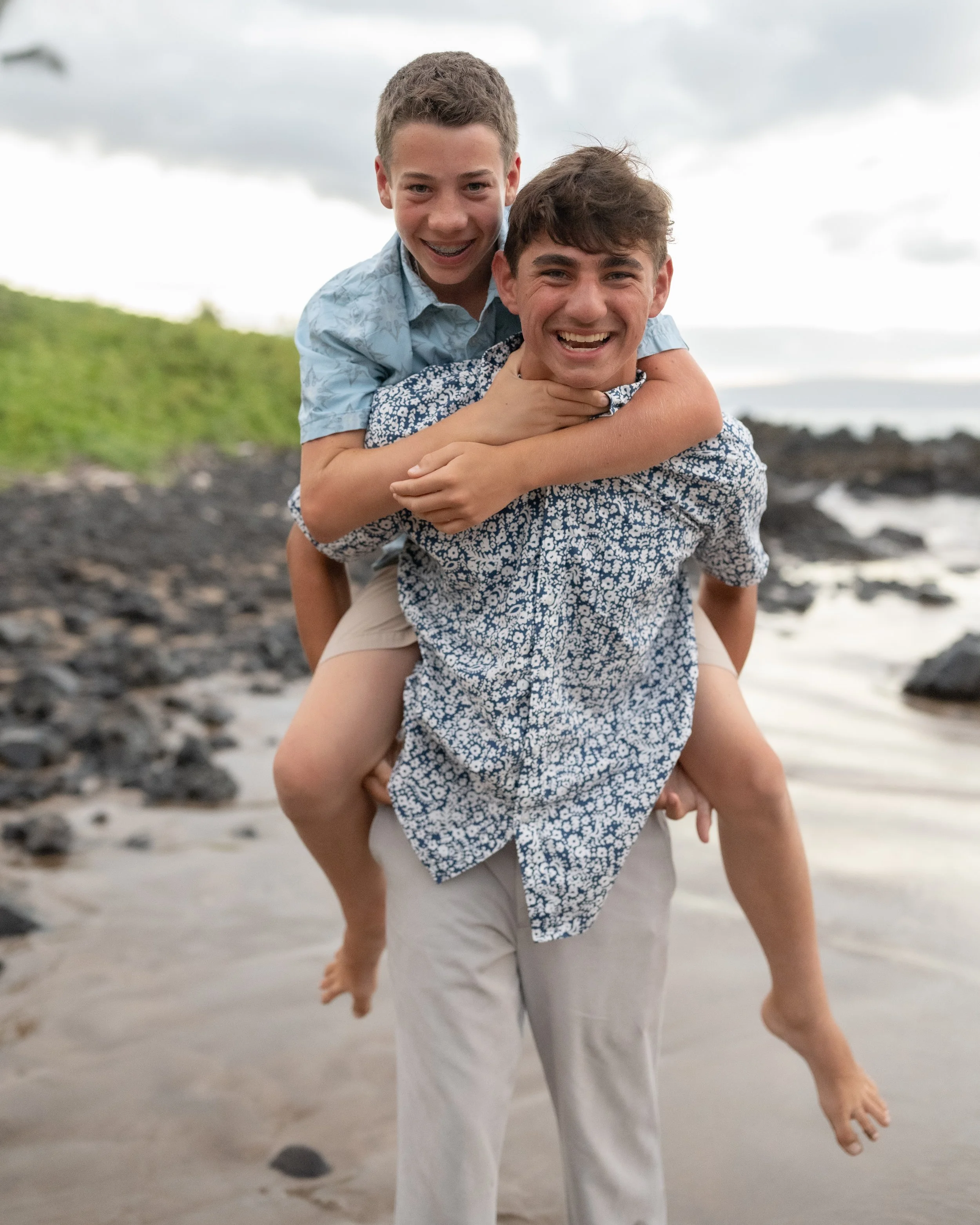 Smiling brothers enjoying a piggyback ride on a Maui beach.
