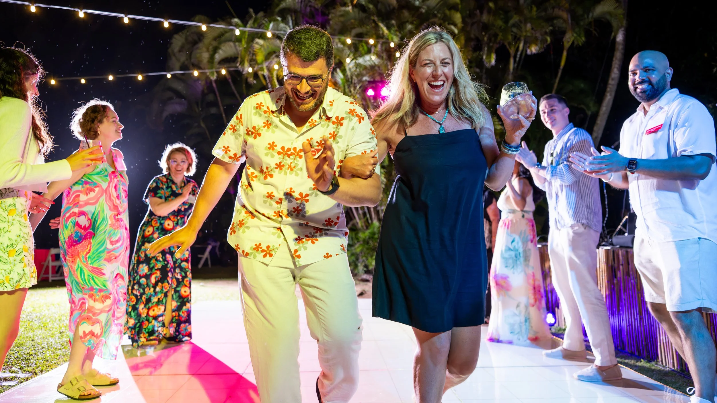 Guests dancing together beneath colorful lights at an evening celebration.