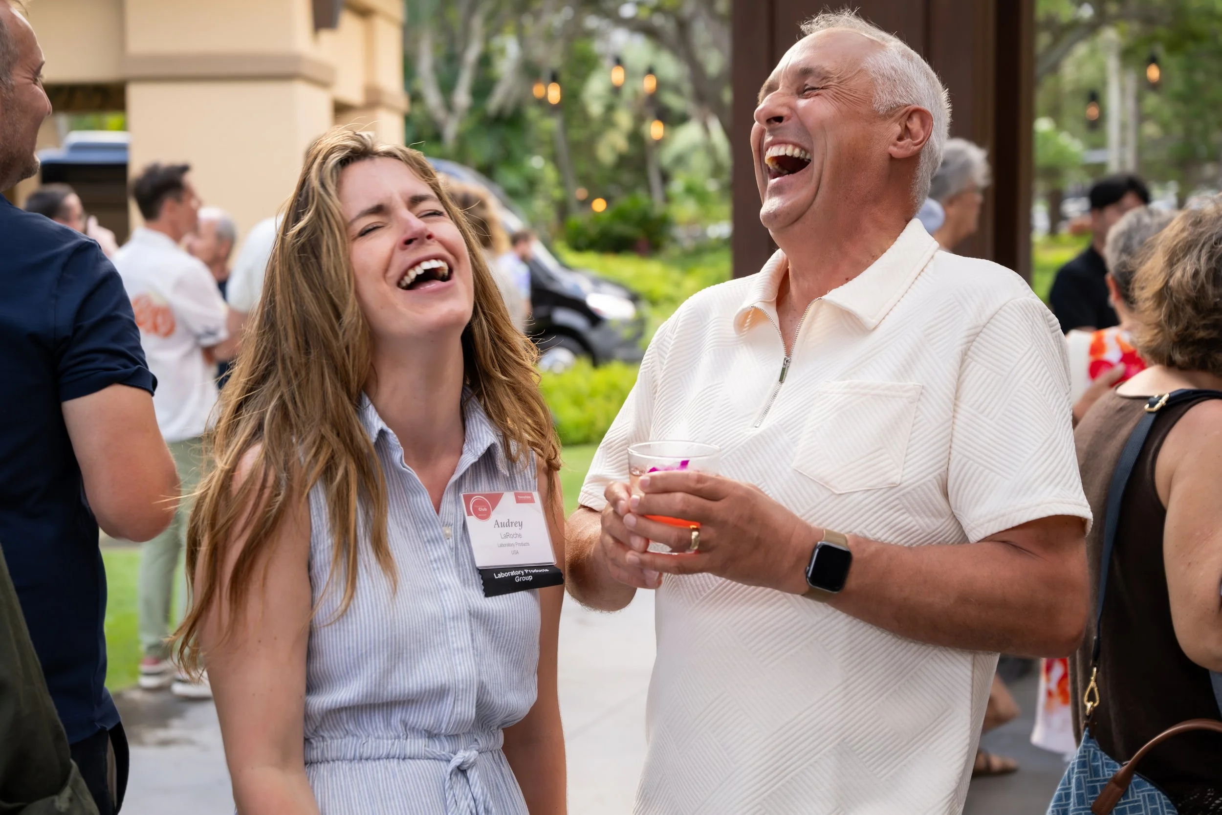 Two guests laughing together while holding drinks at an outdoor reception.