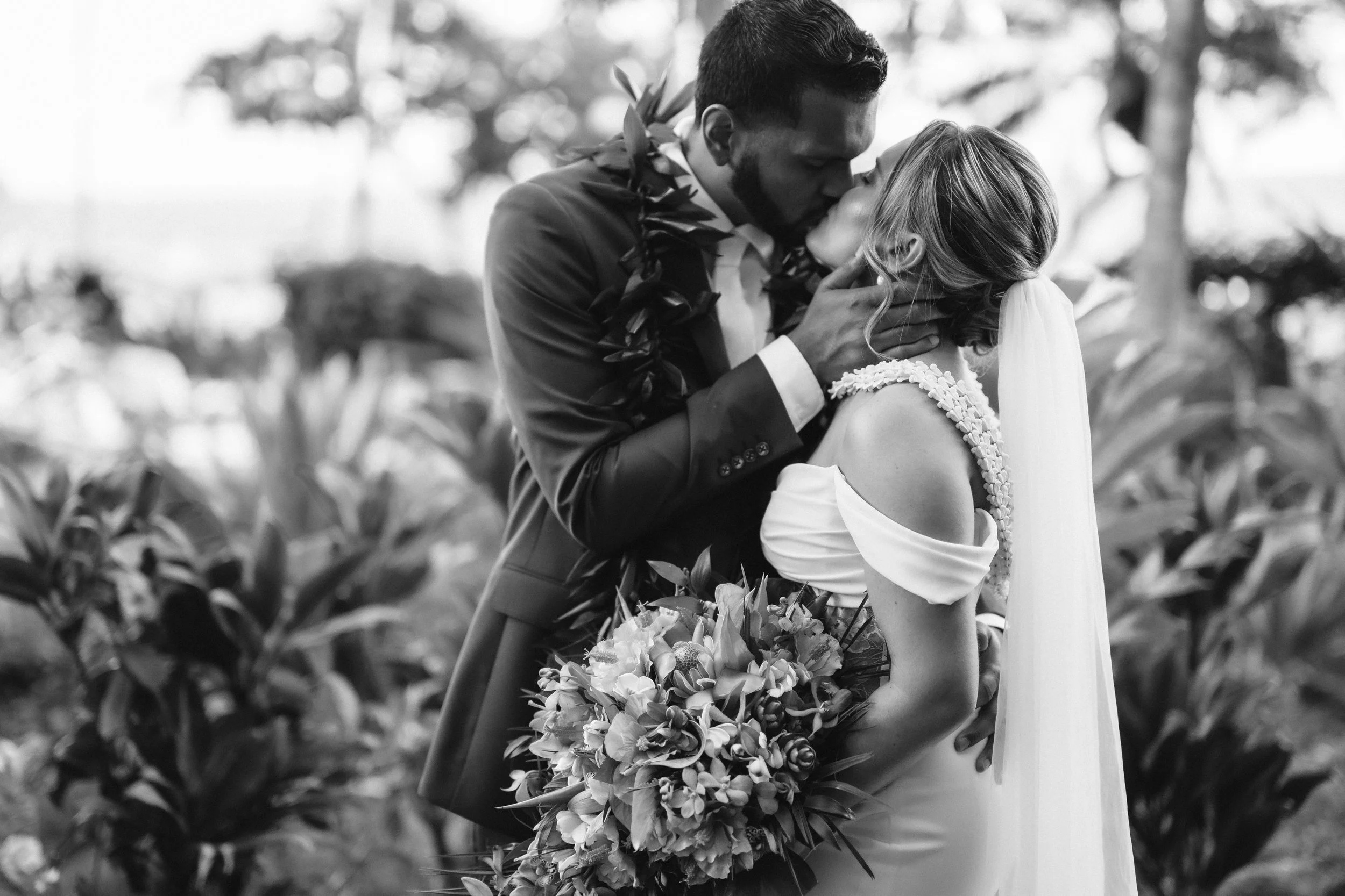 Black-and-white portrait of the groom kissing the bride’s forehead as she holds her bouquet.
