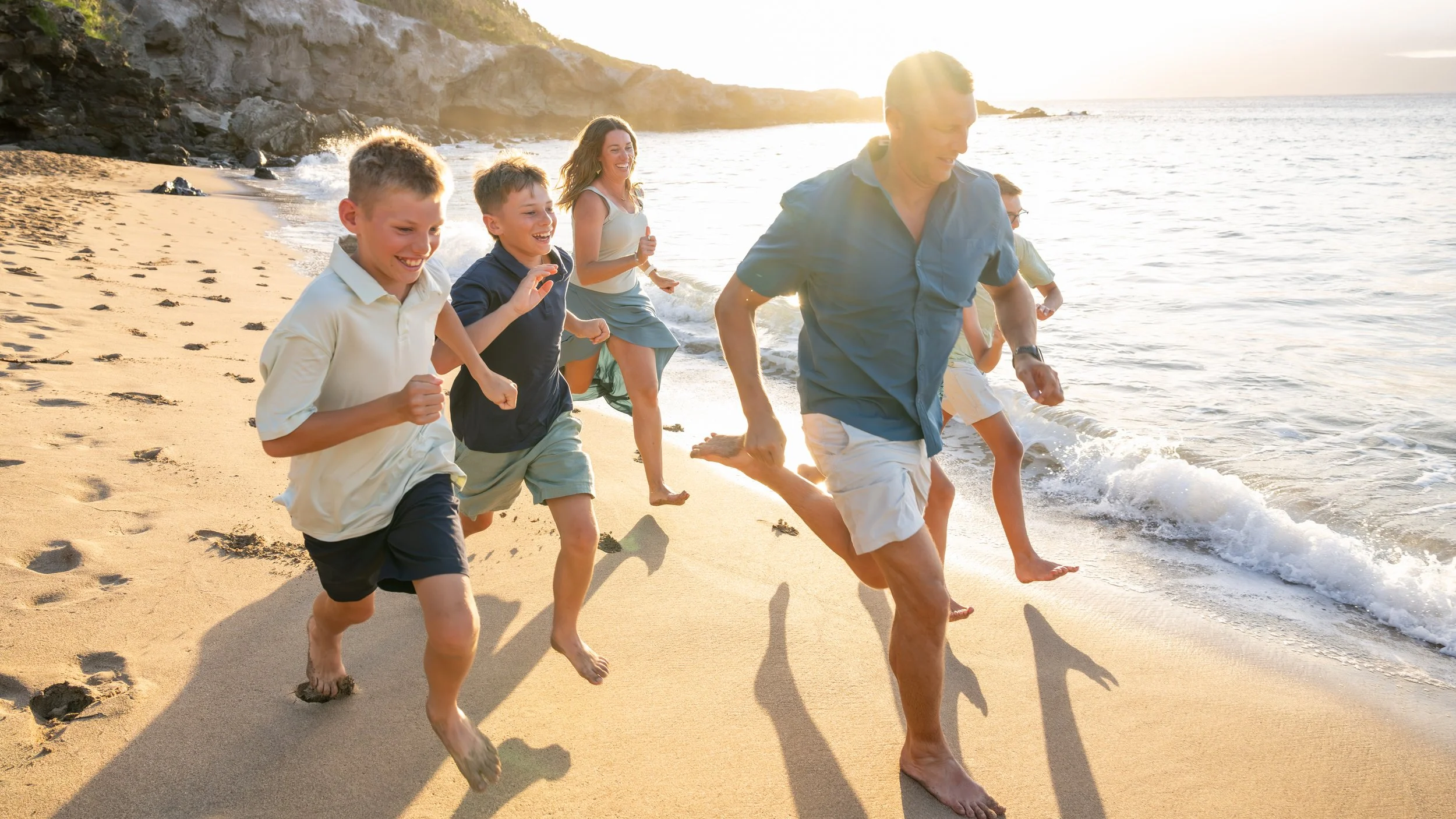 Family laughing and running along the shoreline in the warm evening light on Maui.
