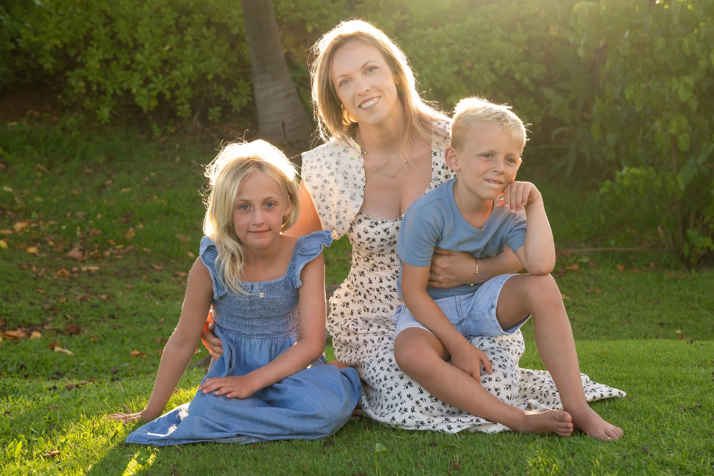 Mother sitting on the grass with her two children in warm afternoon sunlight.
