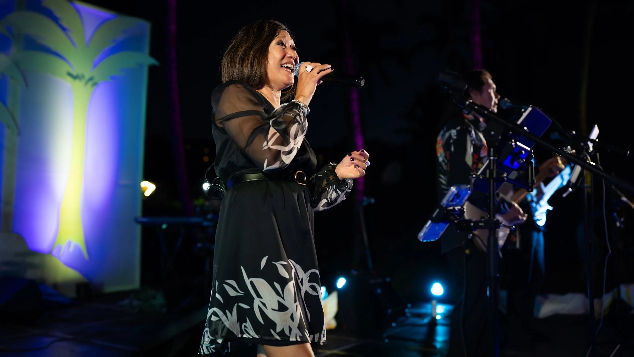 Singer performing with a live band on a stage lit in blue and purple.