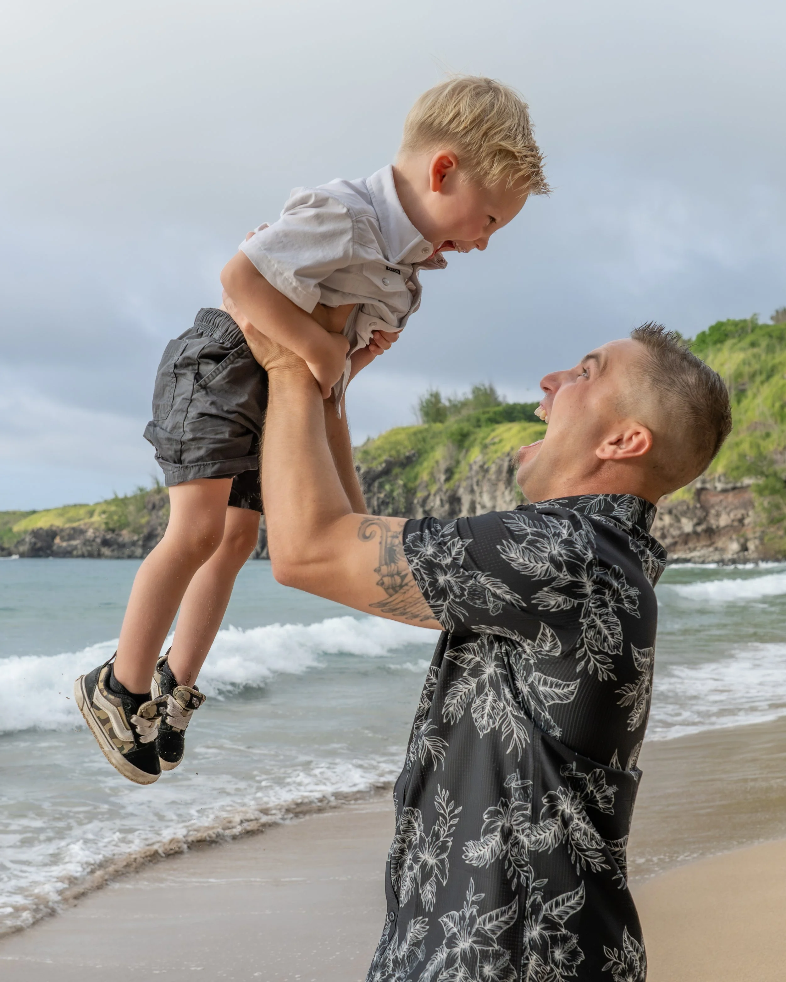 Father lifting his smiling son into the air beside the ocean.