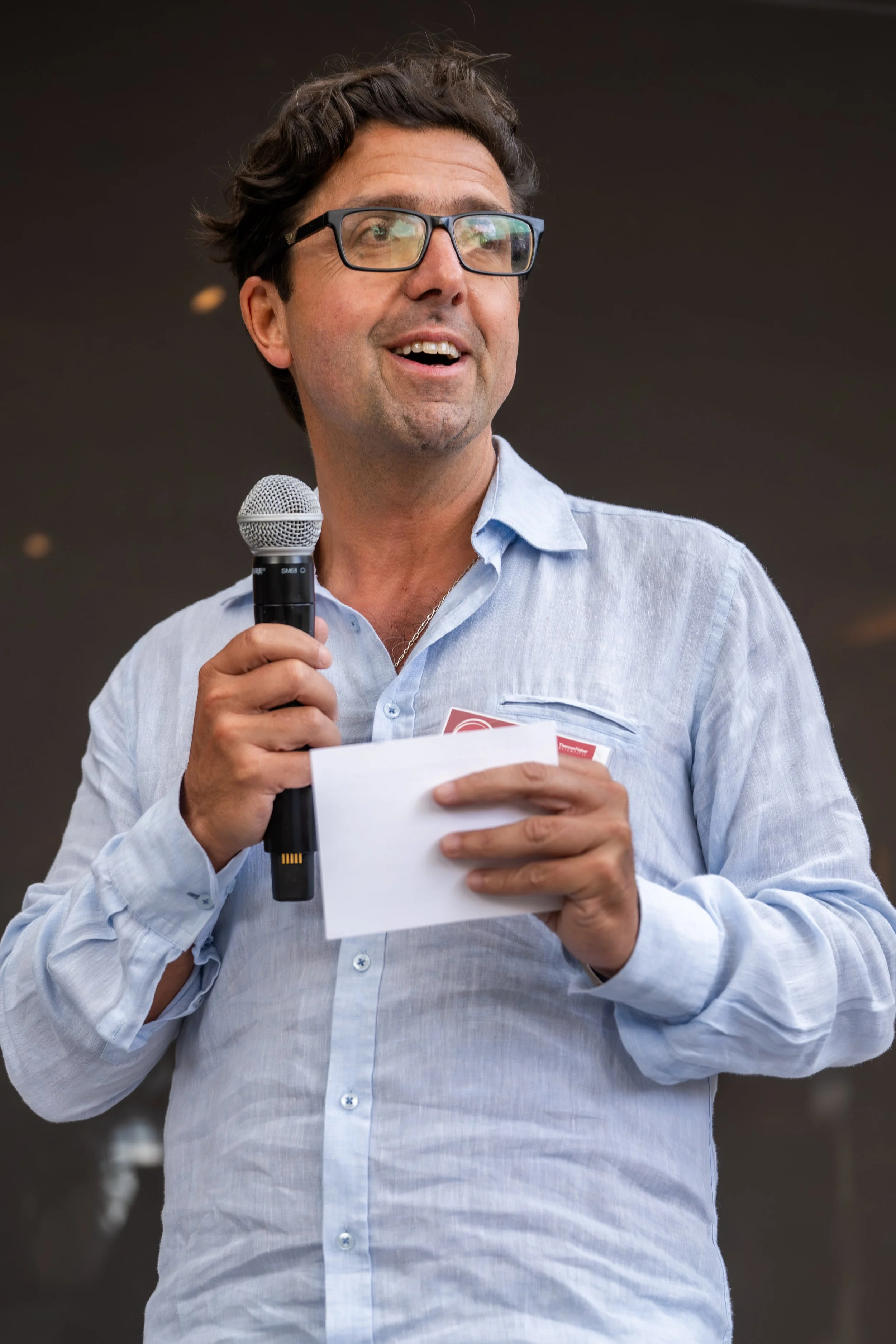 Company leader holding a microphone and note cards while addressing attendees.