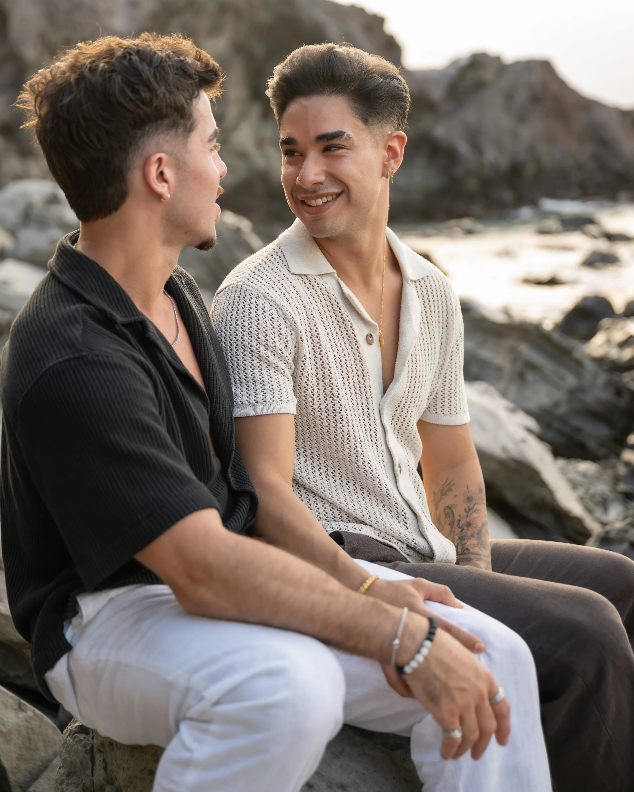 Couple sharing a smile while seated together on lava rocks during a Maui beach portrait session.