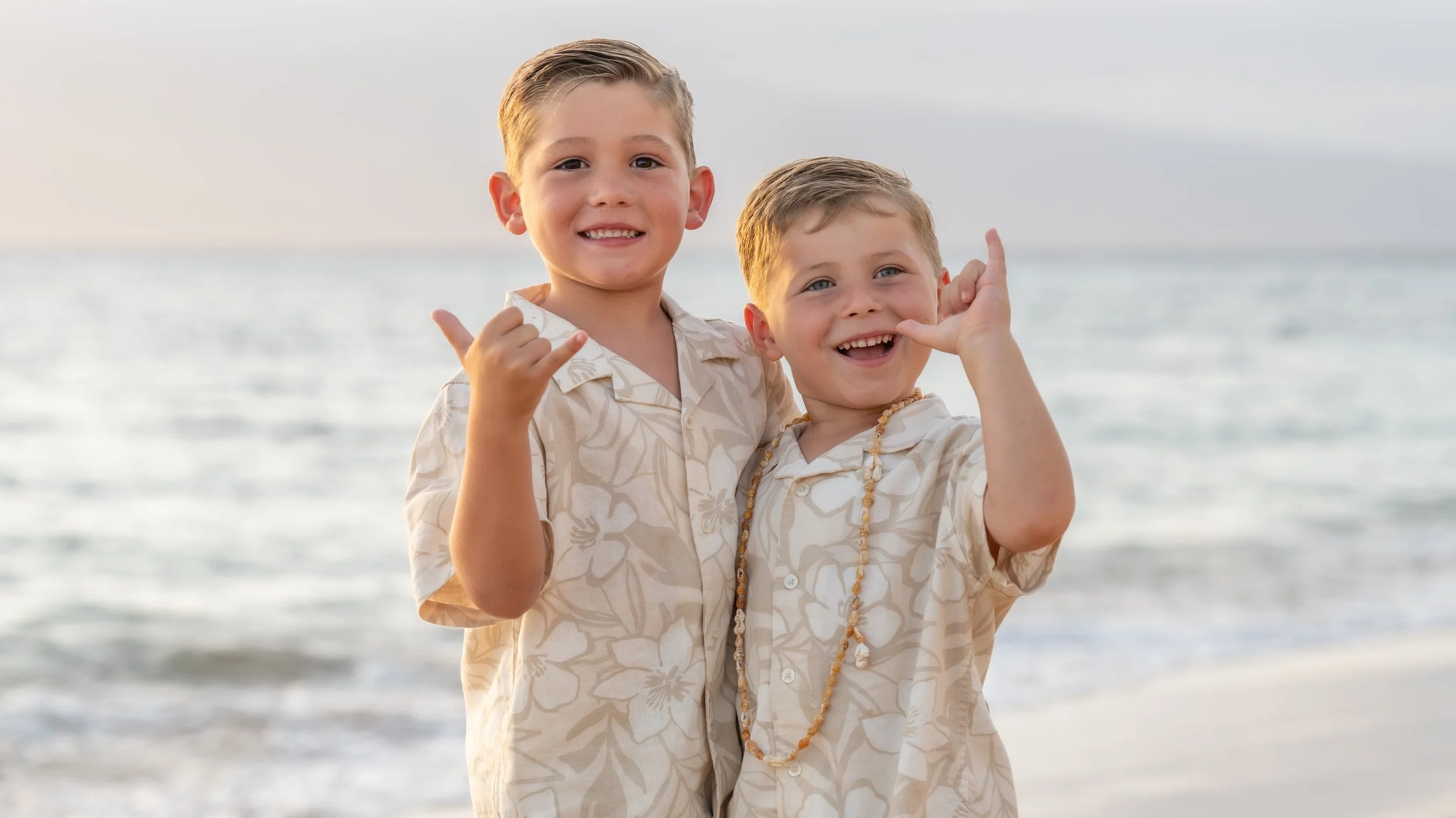 wo smiling brothers in matching tropical shirts making shaka gestures.